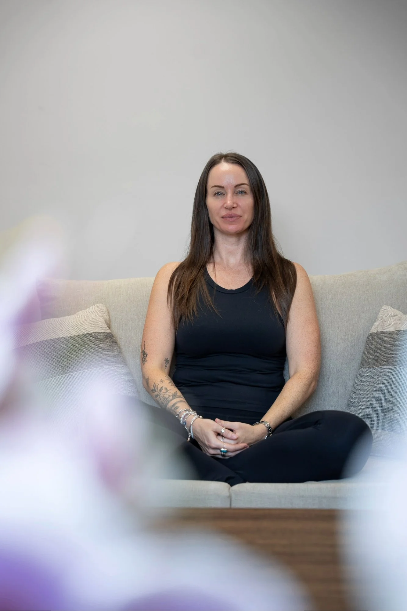 Katie from Kokoro Wellness smiling at the camera while seated in a relaxed meditation position.