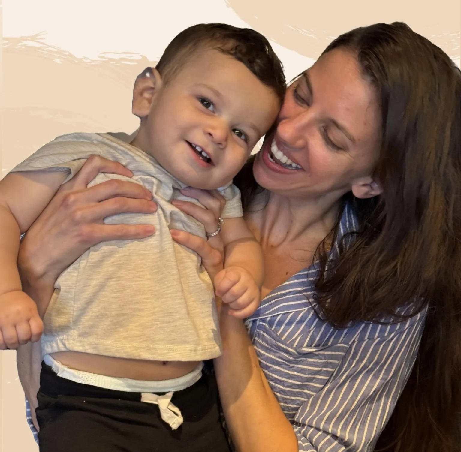 A woman with long dark hair and a striped shirt holds a young boy with short dark hair, both smiling and close to each other.