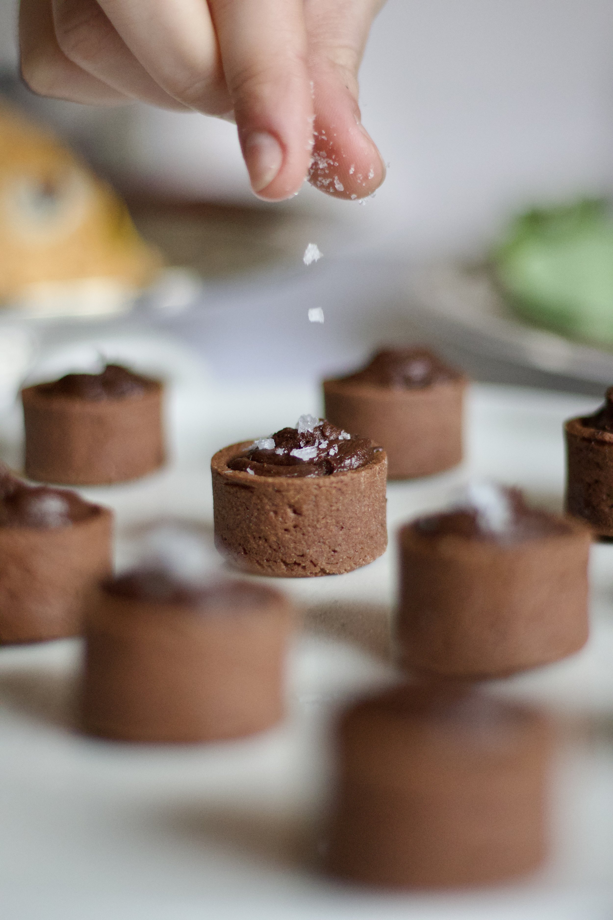 Une main saupoudre du sel sur des mini-tartes au chocolat.