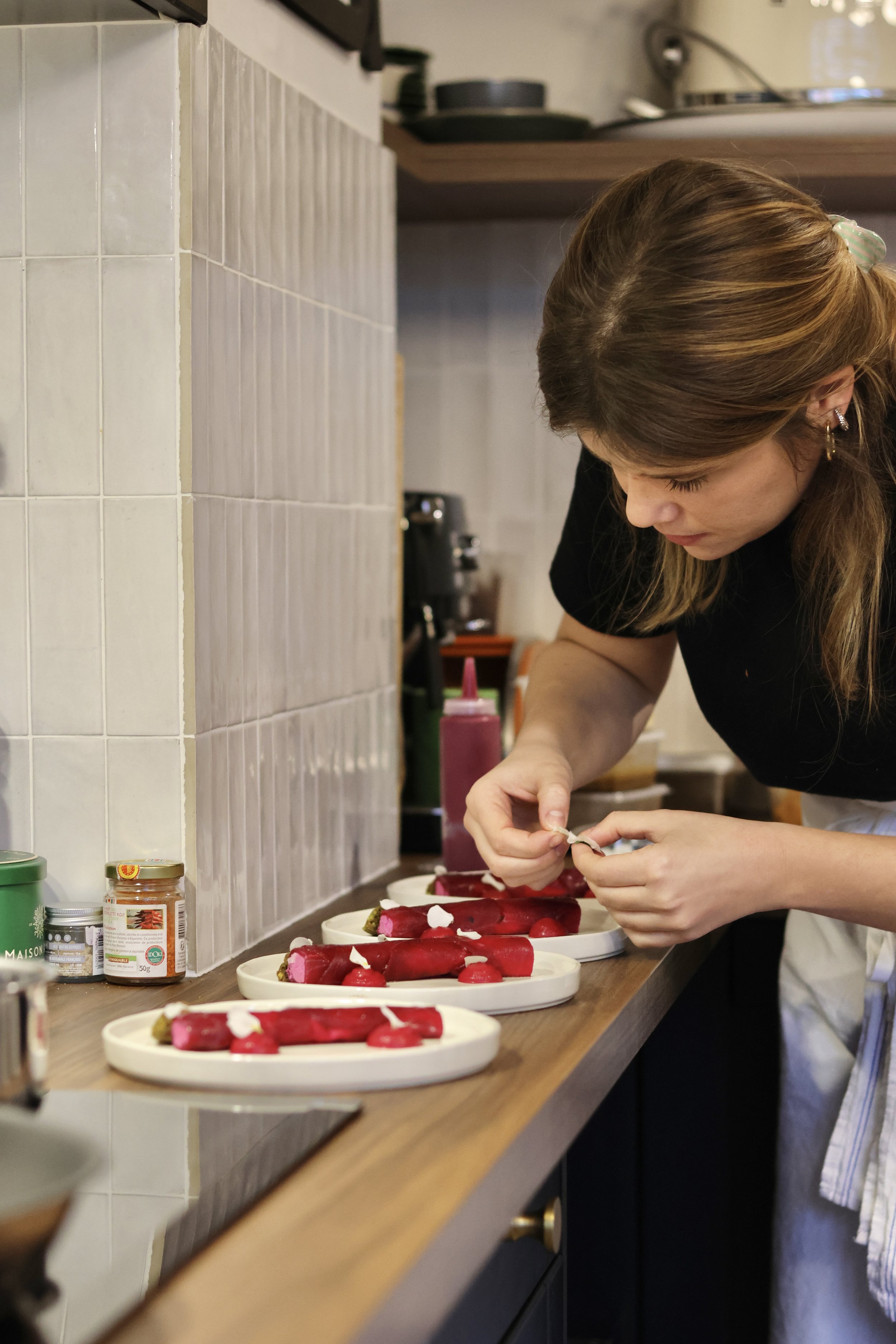 Une femme prépare des tartines de radis sur des assiettes blanches dans une cuisine.