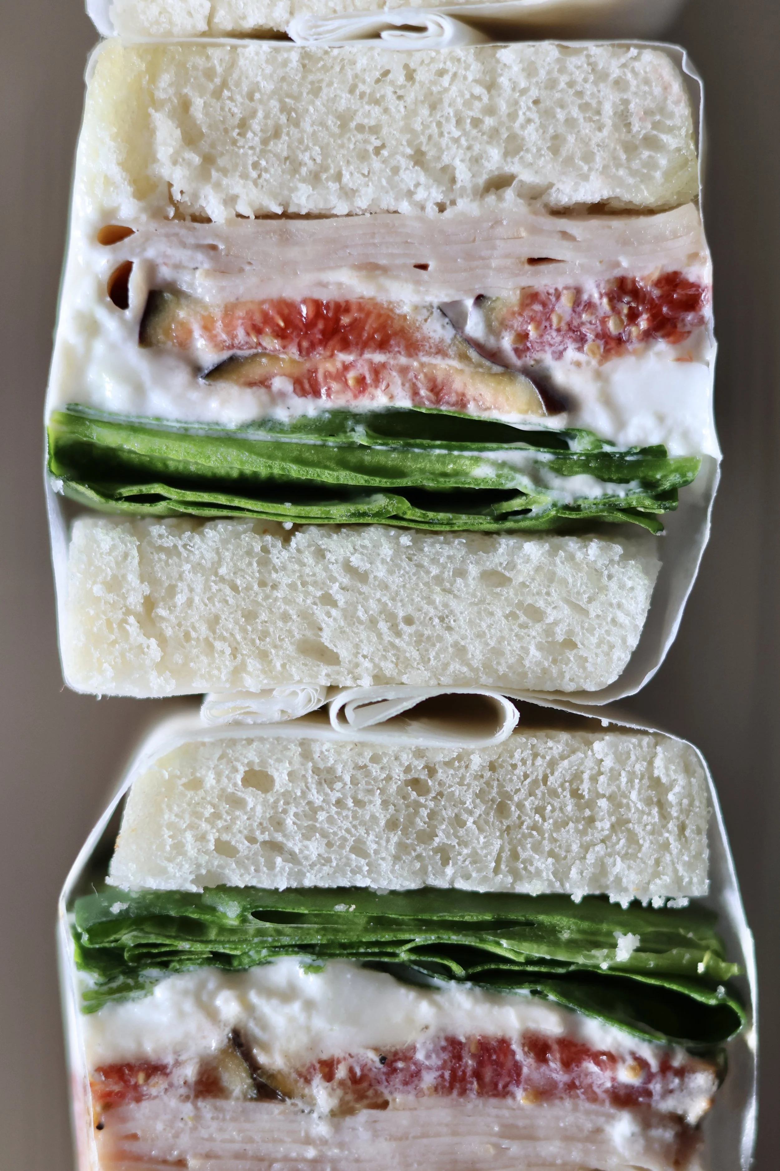 Vues en coupe de deux sandwiches avec des couches de pain blanc, de la salade verte, des tomates, du fromage et de la viande.