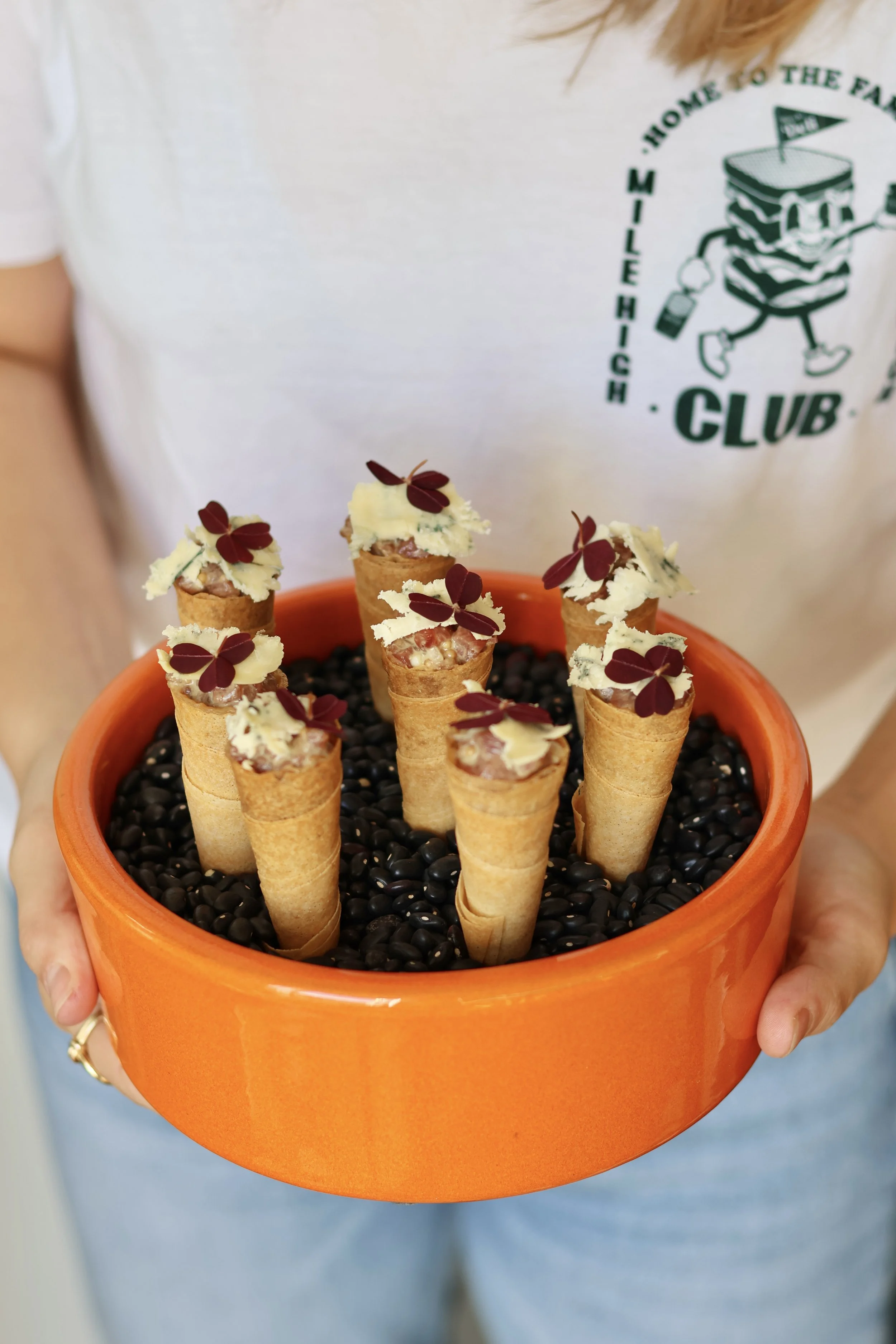Une personne tient un bol orange rempli de haricots noirs avec des cornets de glace garnis de chocolat blanc et de petites feuilles rouges décoratives.