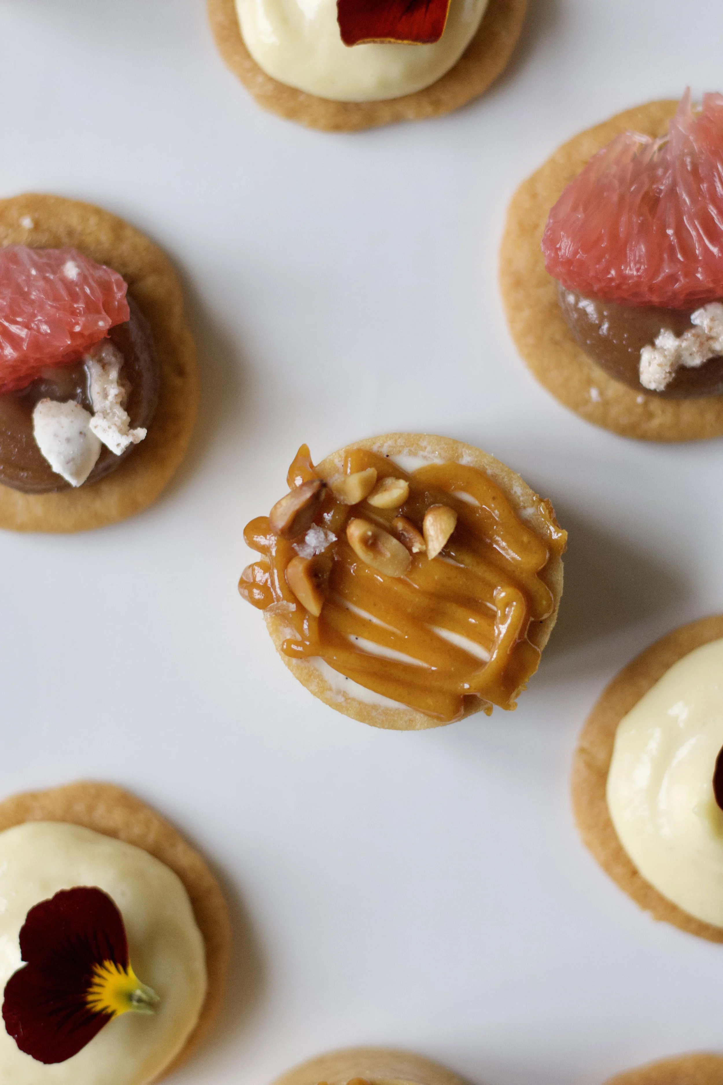 Une sélection de petits biscuits décorés avec du chocolat, des fruits et des garnitures variées.