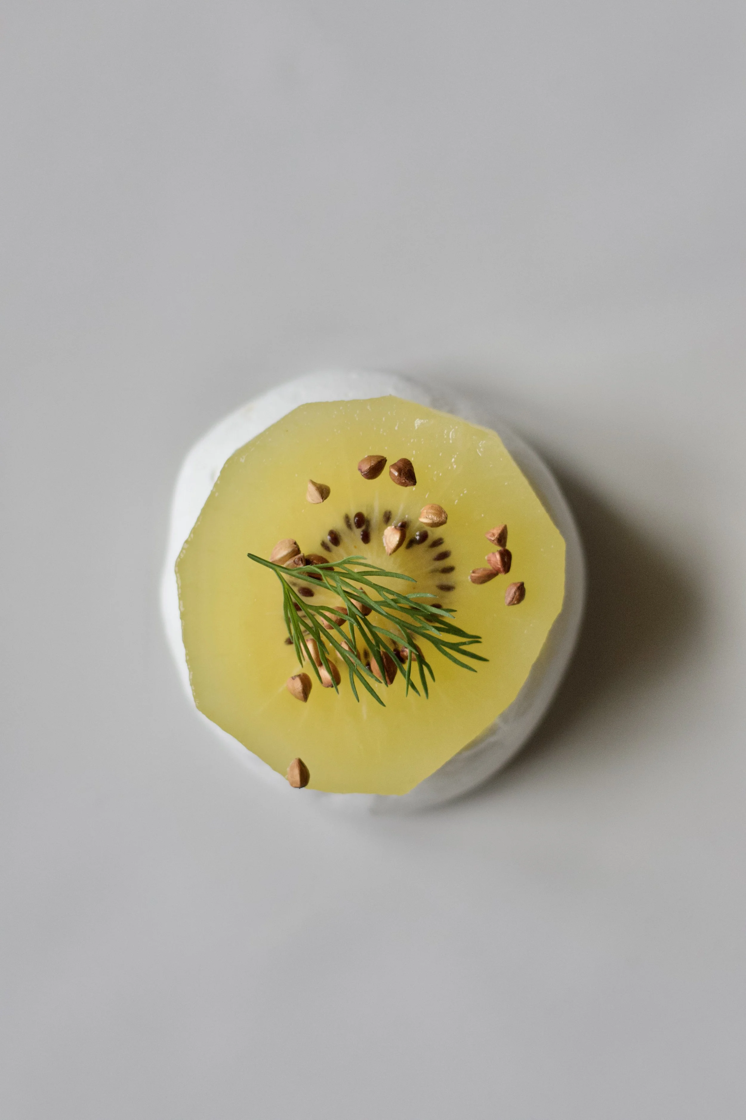 Une tranche de kiwi garnie de graines de lin et d'une branche de ciboulette, posée sur une surface blanche.