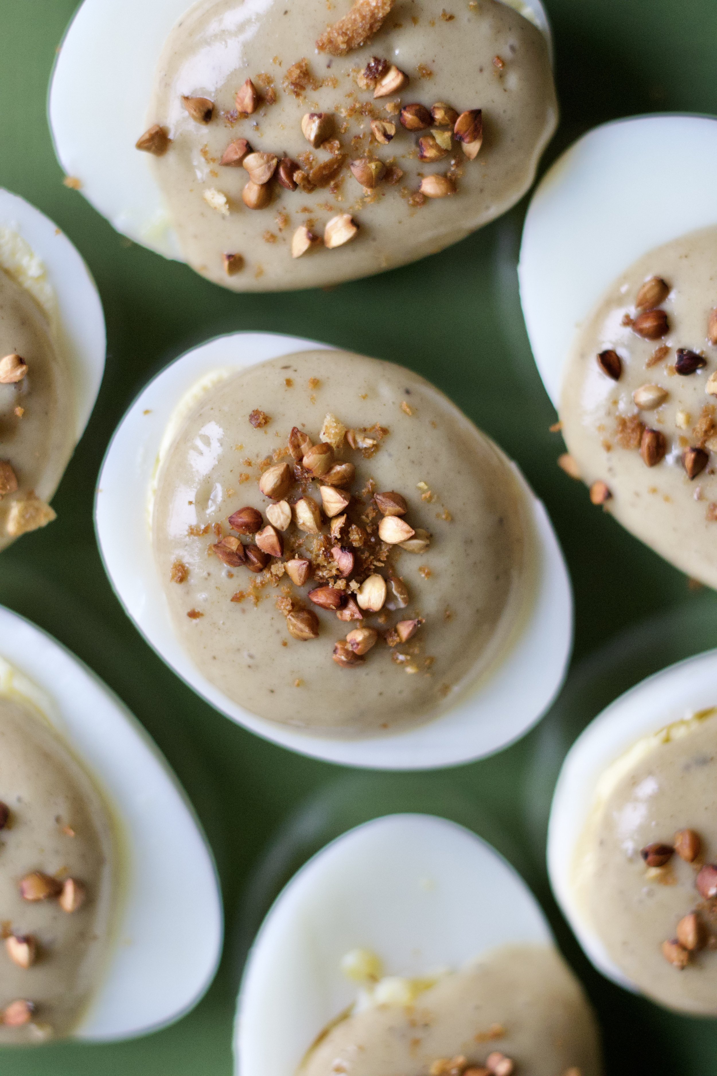 Œufs de caille farcis avec une garniture beige et garniture de noisettes hachées sur le dessus, servis dans des coques blanches.
