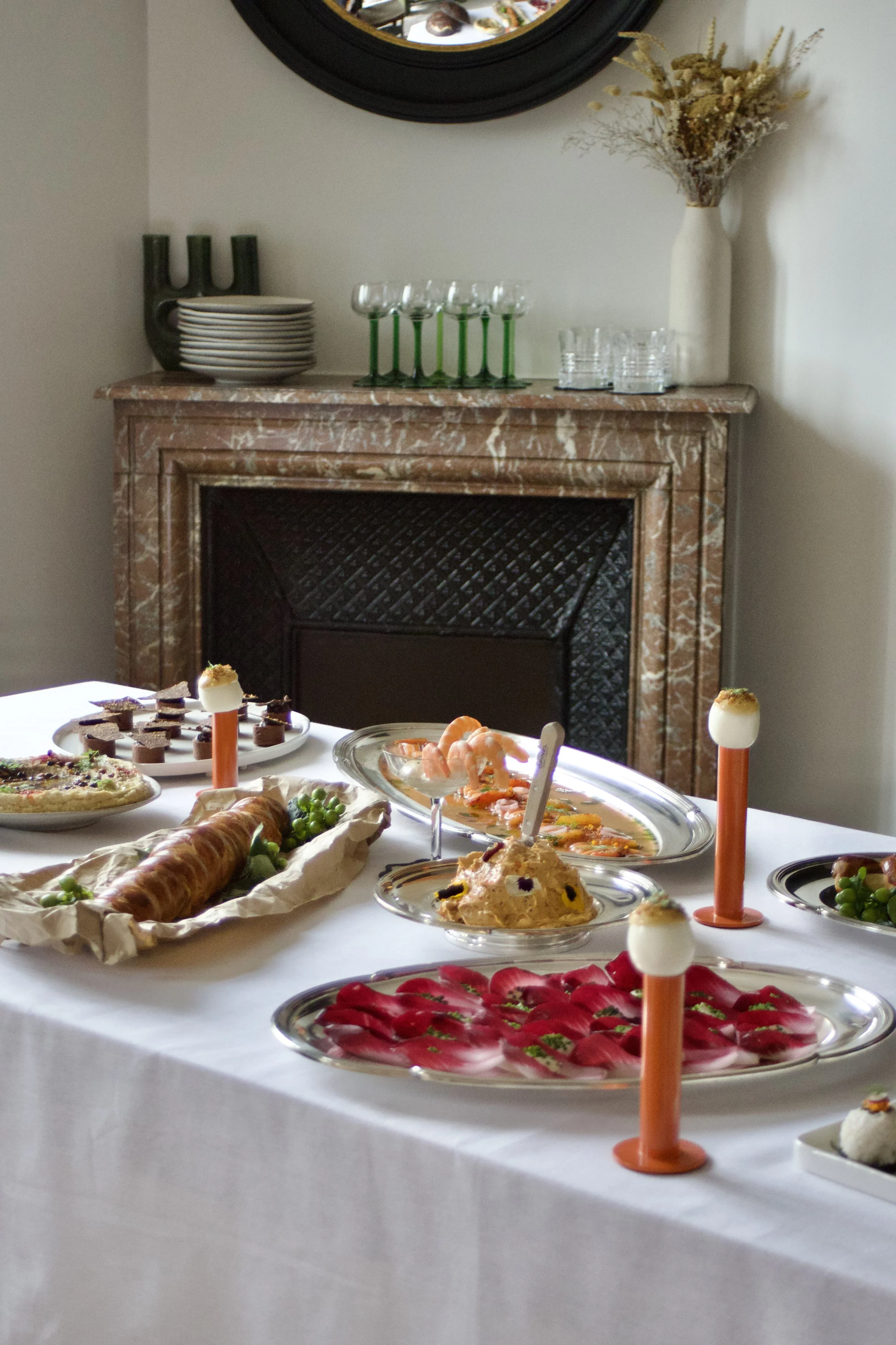 Un buffet de nourriture avec diverses assiettes de plats et de desserts, décoré pour une occasion spéciale dans une pièce avec cheminée en marbre et vase avec des fleurs.