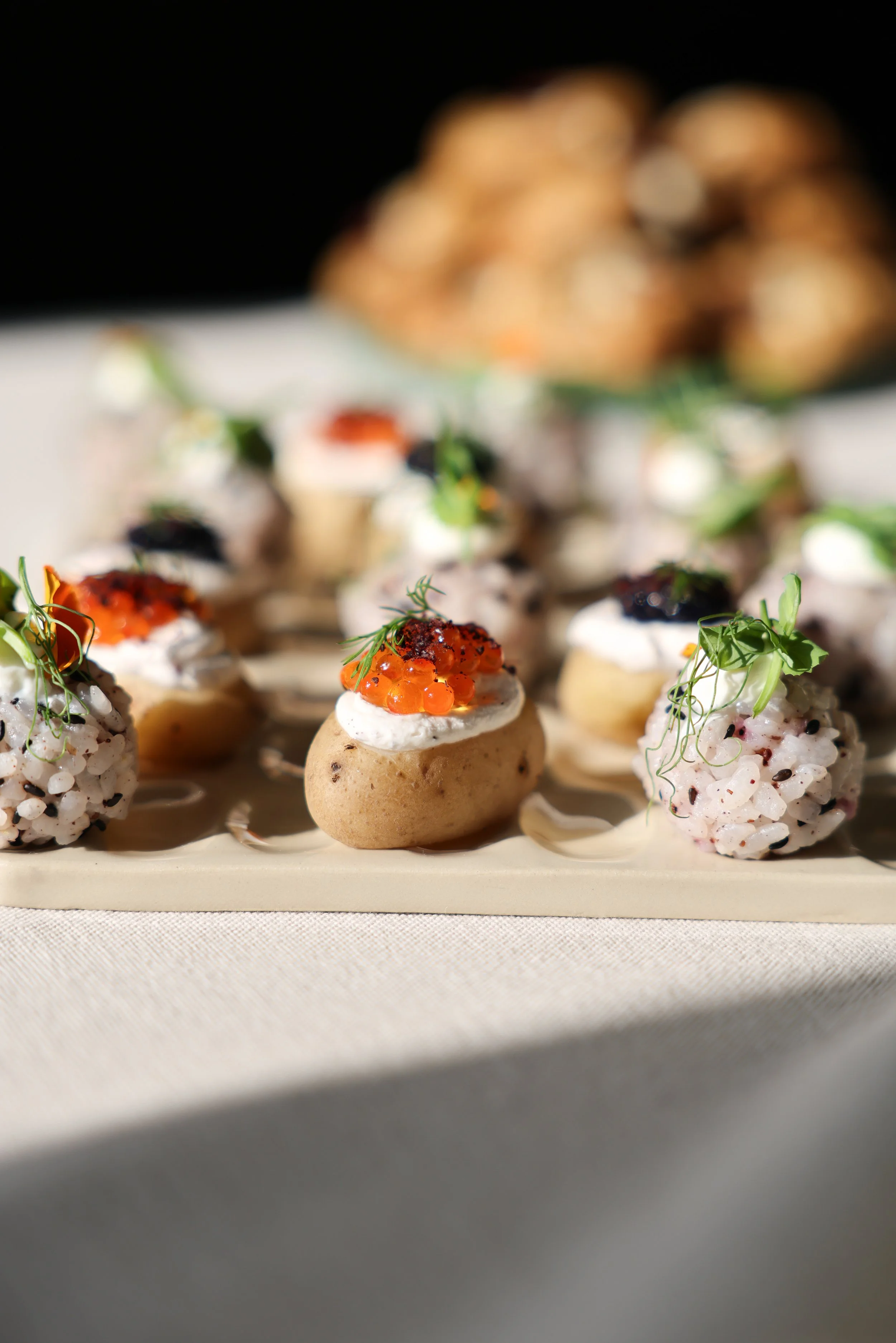 Assortiment de bouchées gastronomiques présentées sur une planche, avec des garnitures délicates et des herbes fraîches, en avant-plan, un fond flou d'amuse-bouches ou de tapas.