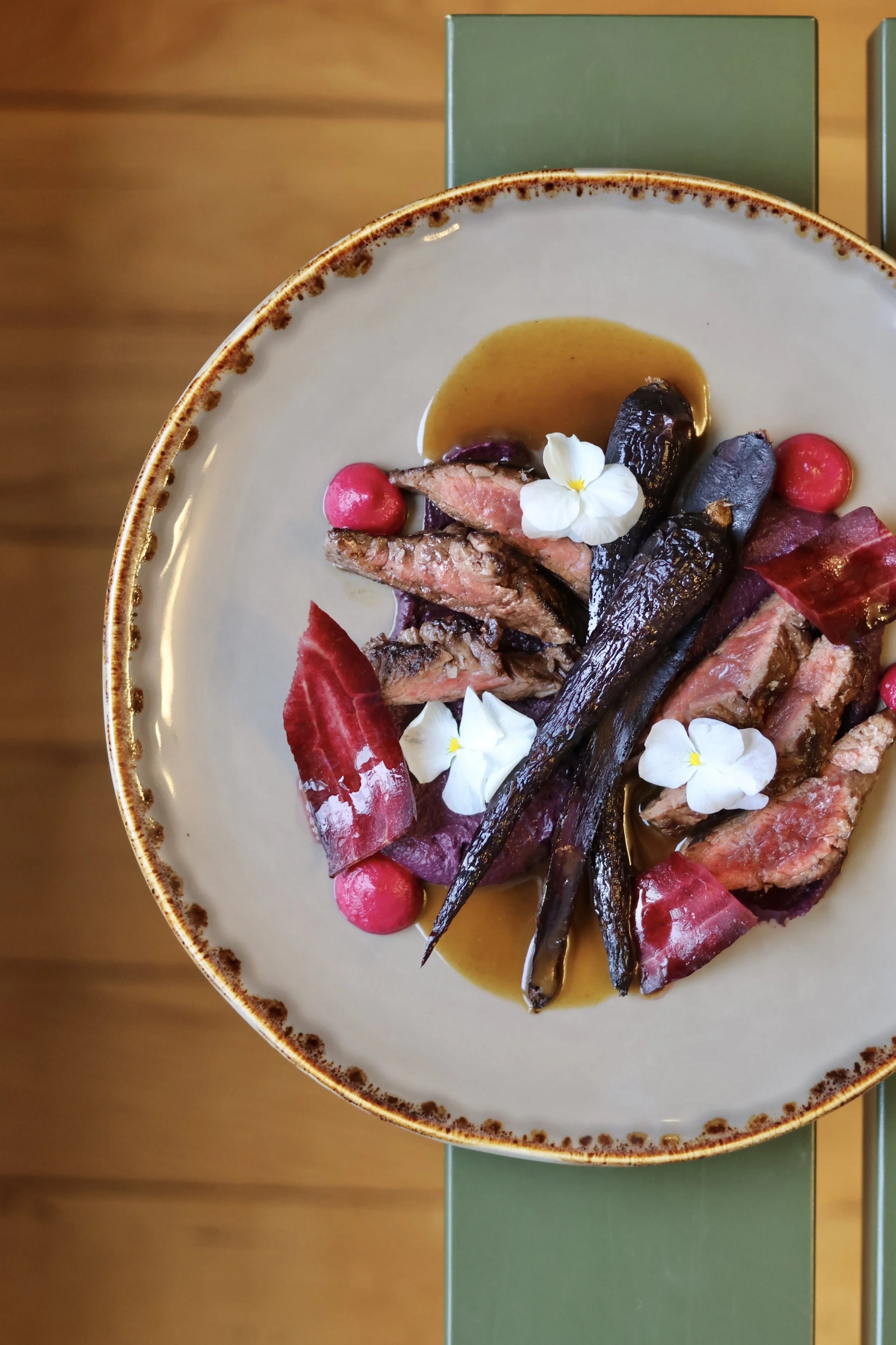 Assiette avec du steak saignant, des légumes racines, une sauce, des fleurs comestibles et des radis, présentation artistique.