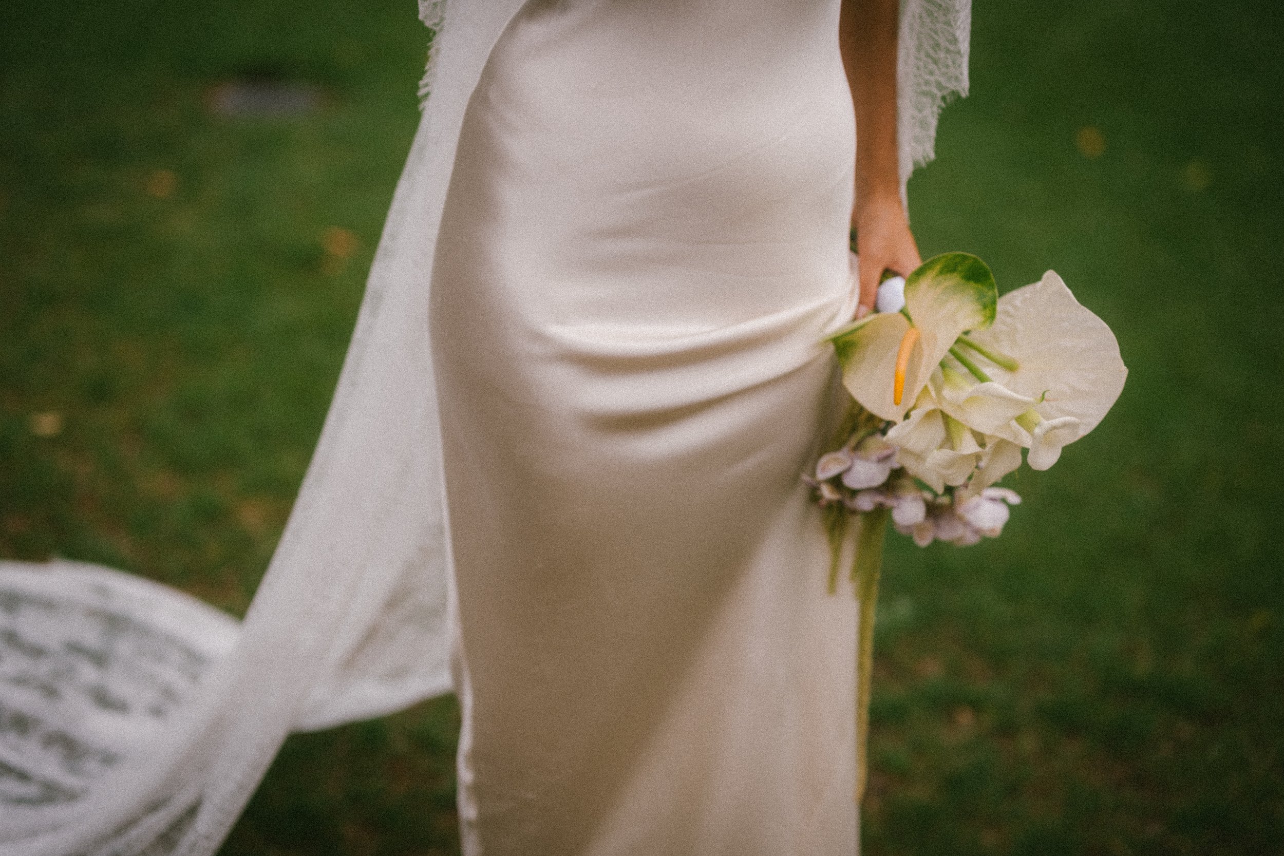 Femme en robe blanche tenant un bouquet de fleurs blanches, prise de près, fond flou de végétation verte.