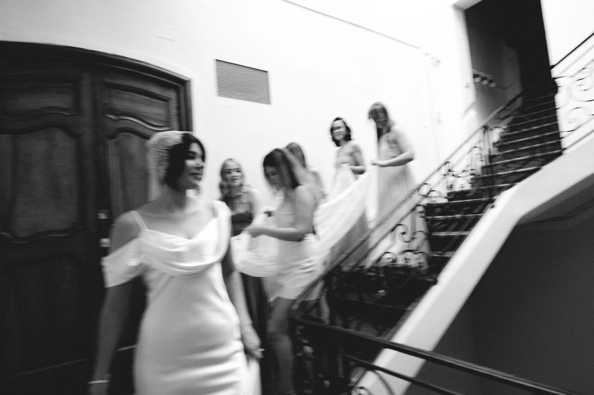 Groupe de femmes habillées en blanc dans une pièce intérieure près d'un escalier en fer forgé.