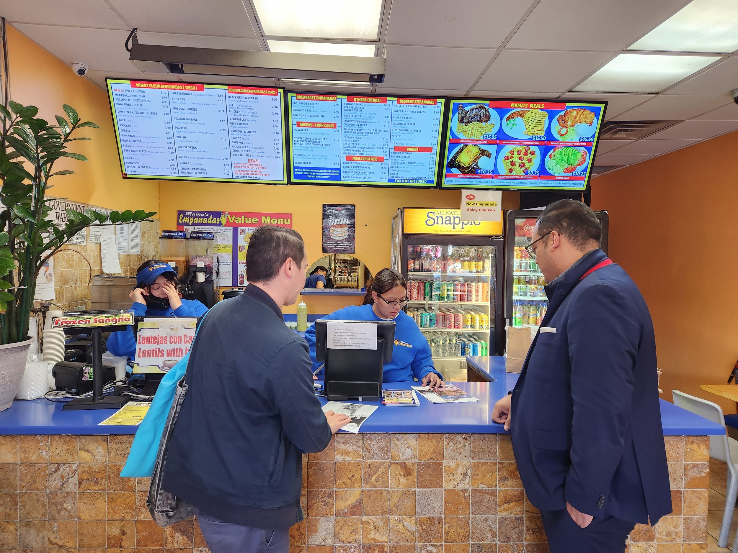  Two men speak to empanada restaurant counter clerk. 