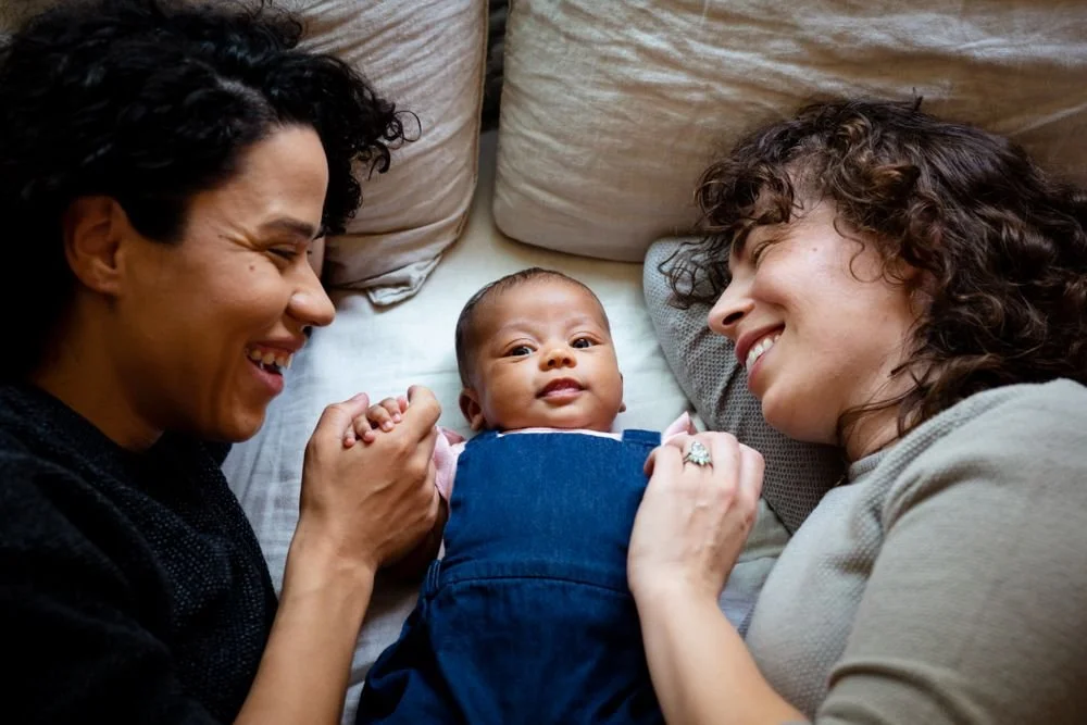 Two moms are laying with baby.