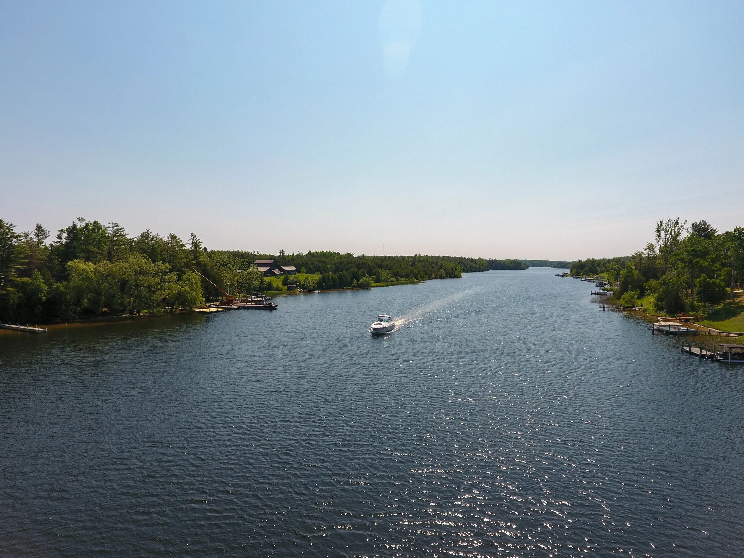 Drone view of the Black River in Cheboygan Michigan surrounded by trees, waterfront properties, and calm Northern Michigan water.