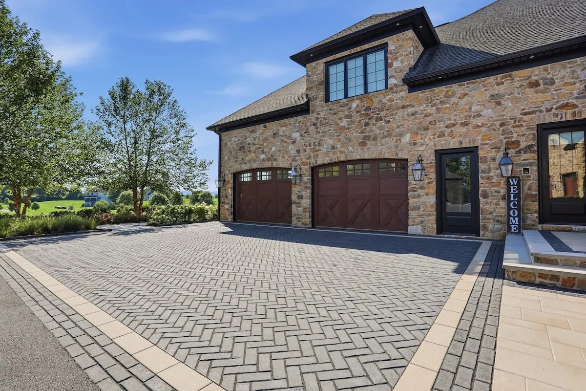 Herringbone paver courtyard leading to a stone home's garage doors — Weaver's Landscape Company