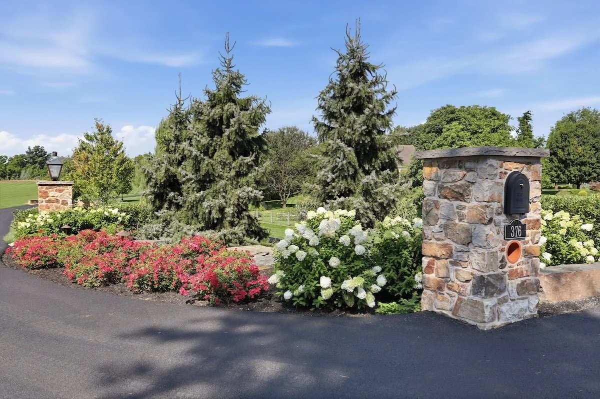 Stone entrance pillar with mailbox lantern flanked by red roses and white hydrangeas — Weaver's Landscape Company