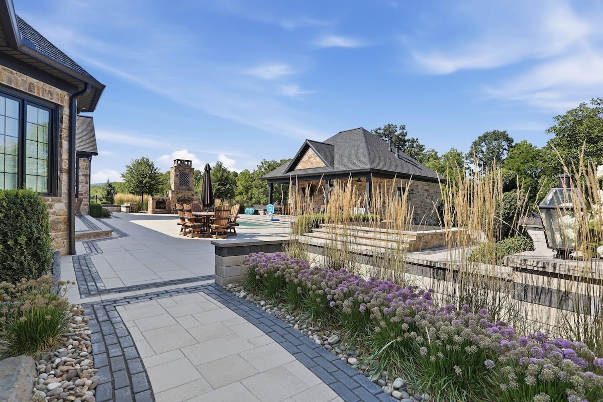 Backyard pool with a stone pool house and covered dining area beyond ornamental grasses — Weaver's Landscape Company