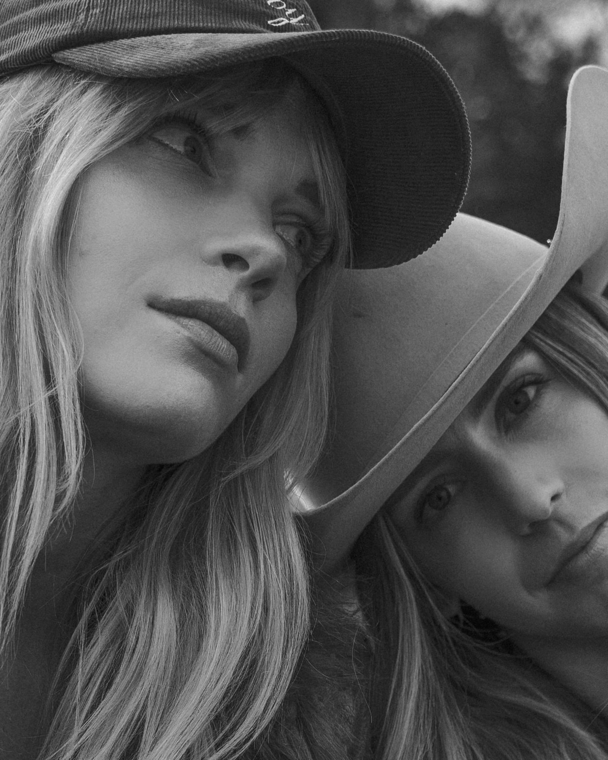 Black and white photo of two women wearing hats, one in a baseball cap and the other in a cowboy hat, looking into the distance.