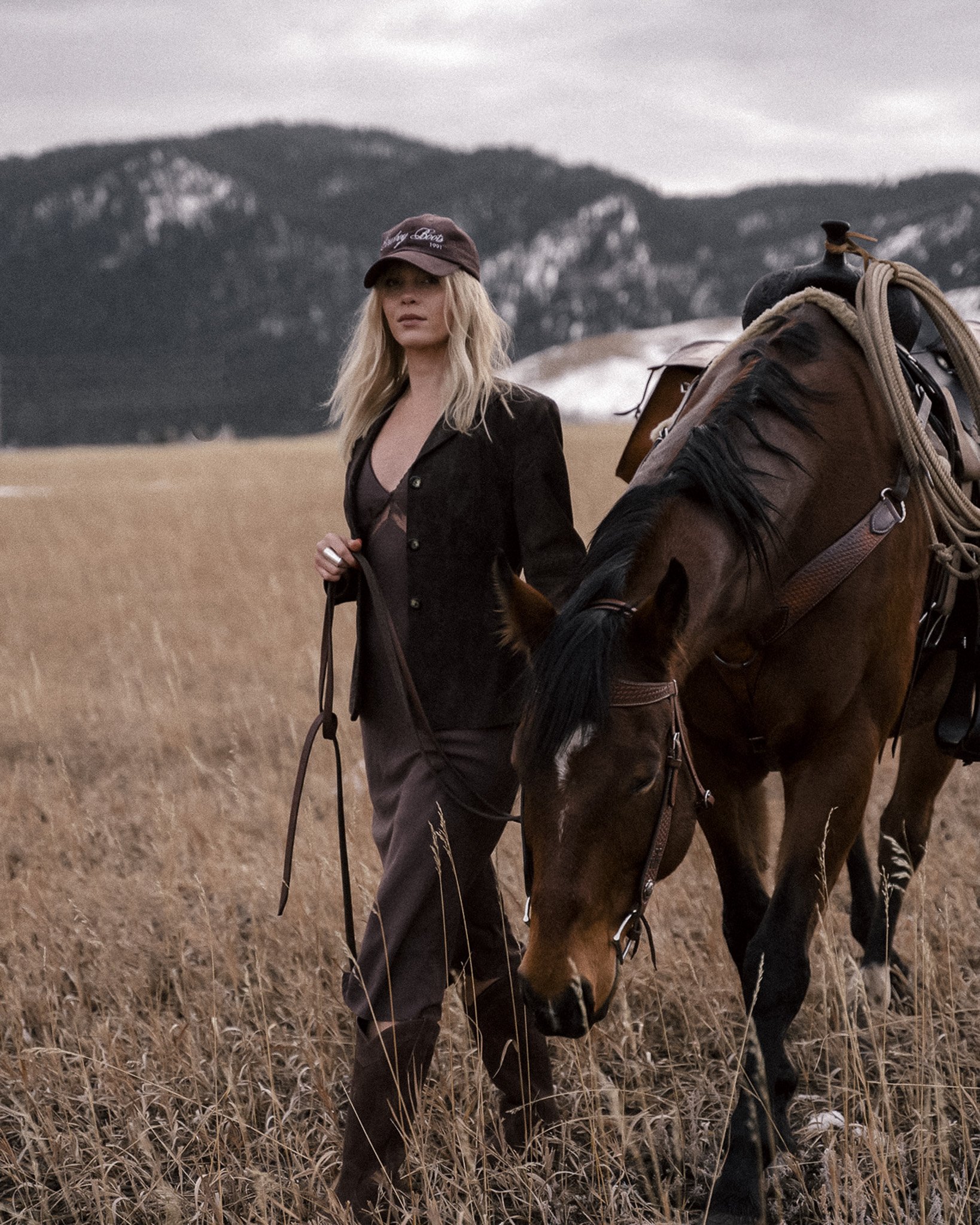 Person walking a horse in a grassy field with mountains in the background.