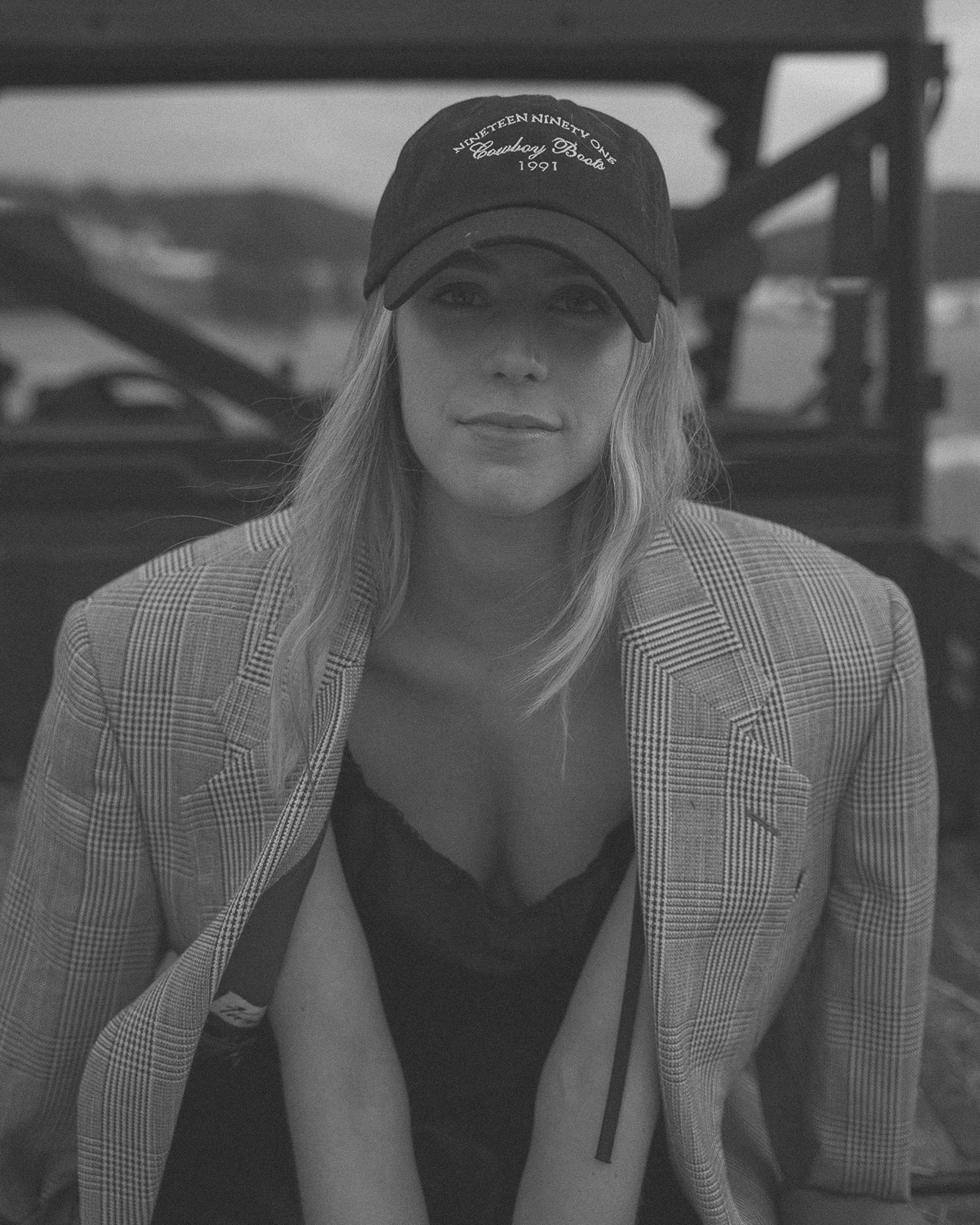 Black and white photo of a woman wearing a checkered blazer and a baseball cap.