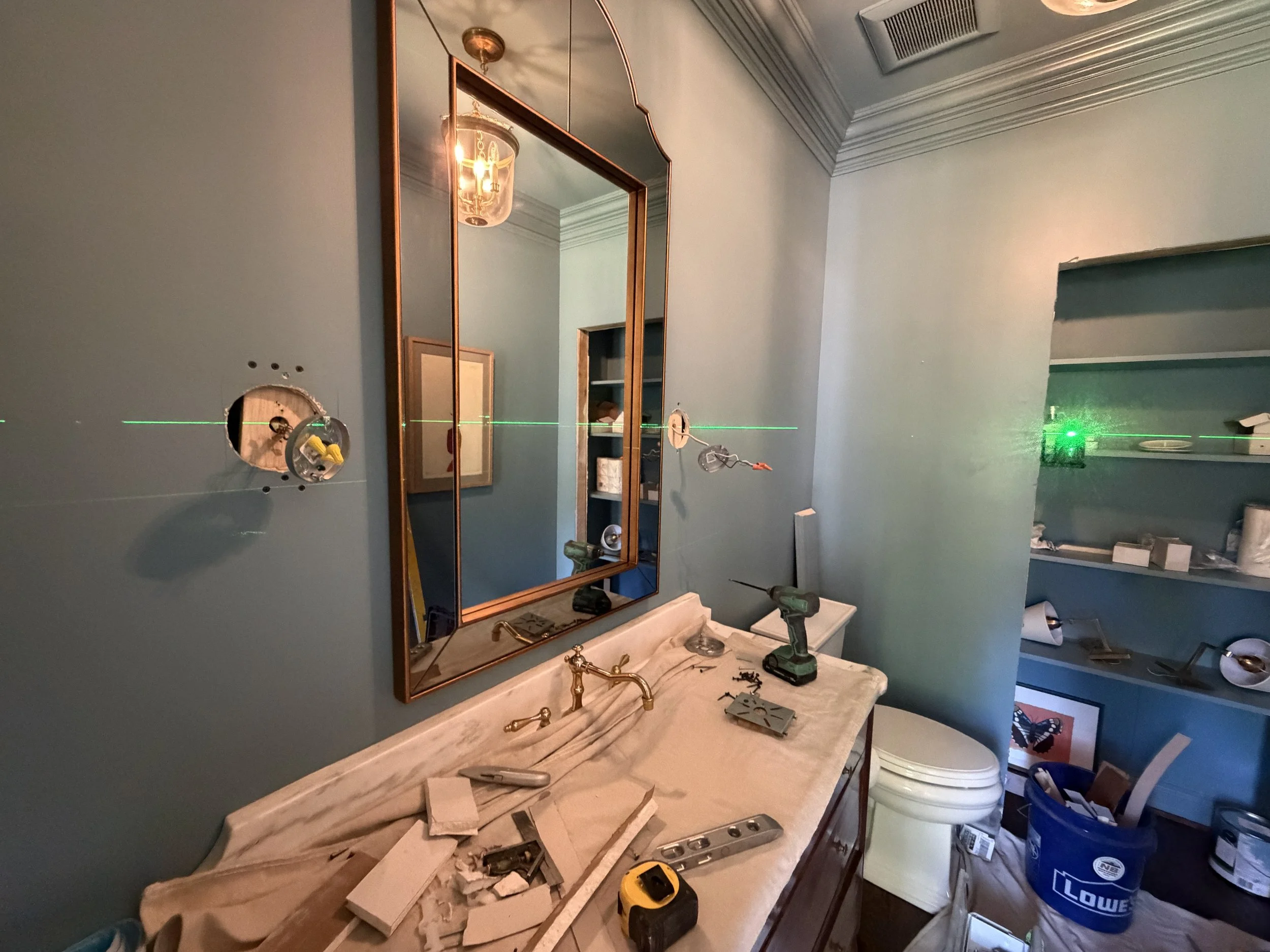 symmetrical wall sconces in the same hand-rubbed antique brass finish are about to be installed in a powder room color drenched in farrow and ball stone blue