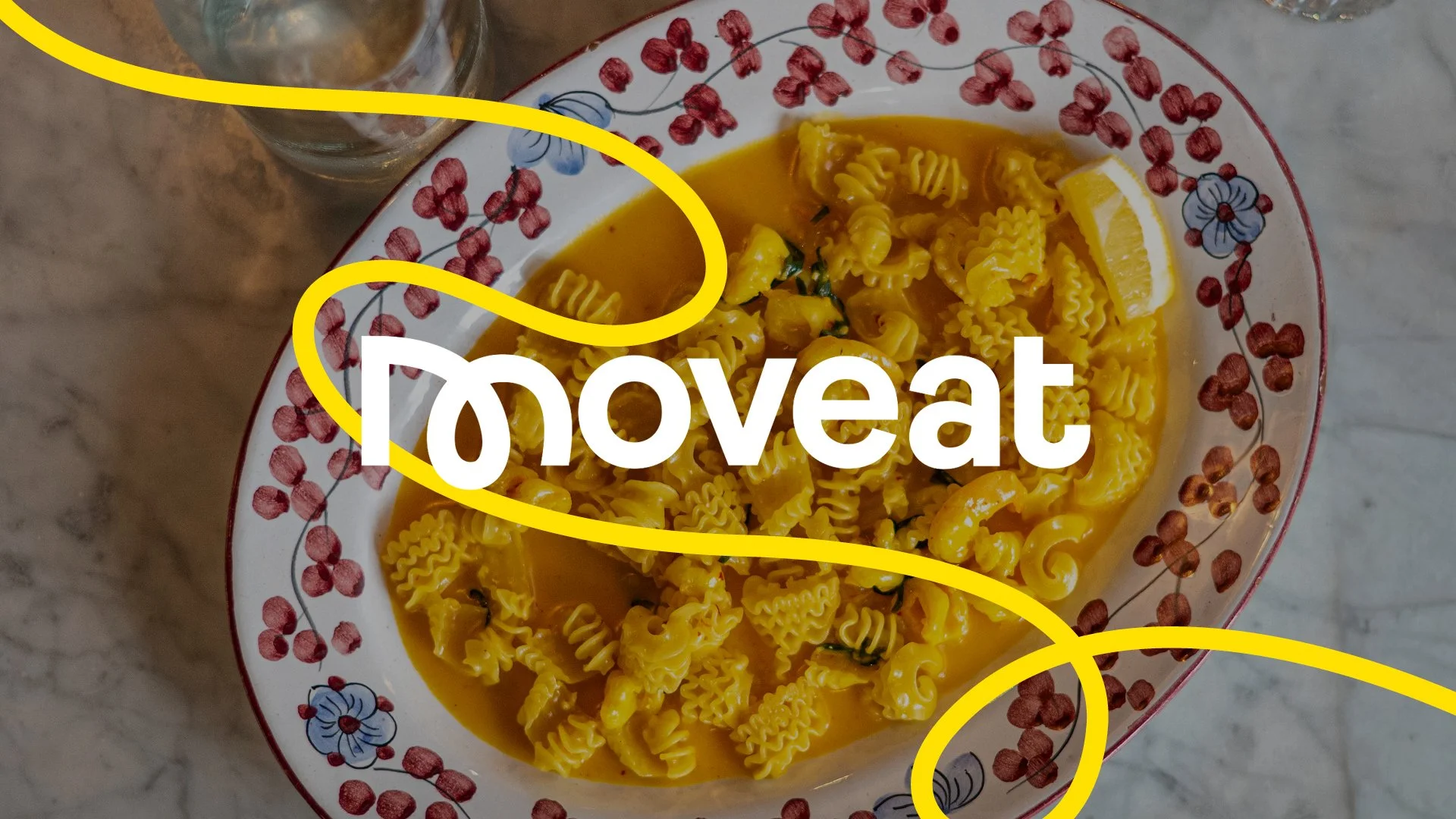 En vit skål med rödblommig kantfärg fyllt med pasta i en gul soppa, serverat på ett marmorbord.