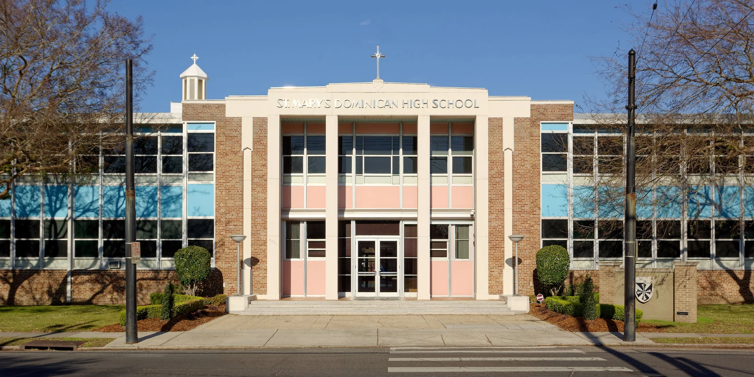 Front view of St. Mary's Dominican High School building with brick and glass facade, steps leading to entrance, and leafless trees on either side.