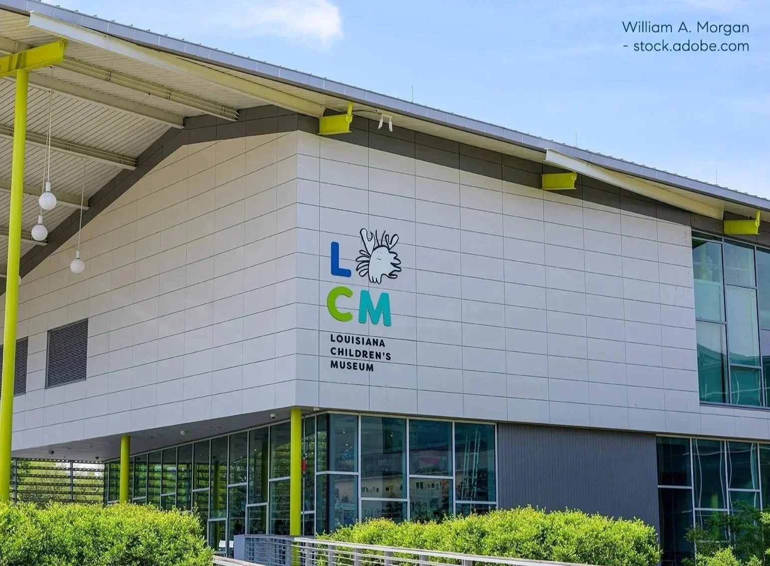 Exterior of the Louisiana Children's Museum building with the logo and name displayed on the wall. The logo features a stylized lion's face with a mane, and the text includes 'L', 'C', and 'M' in blue, green, and cyan respectively, with the full name