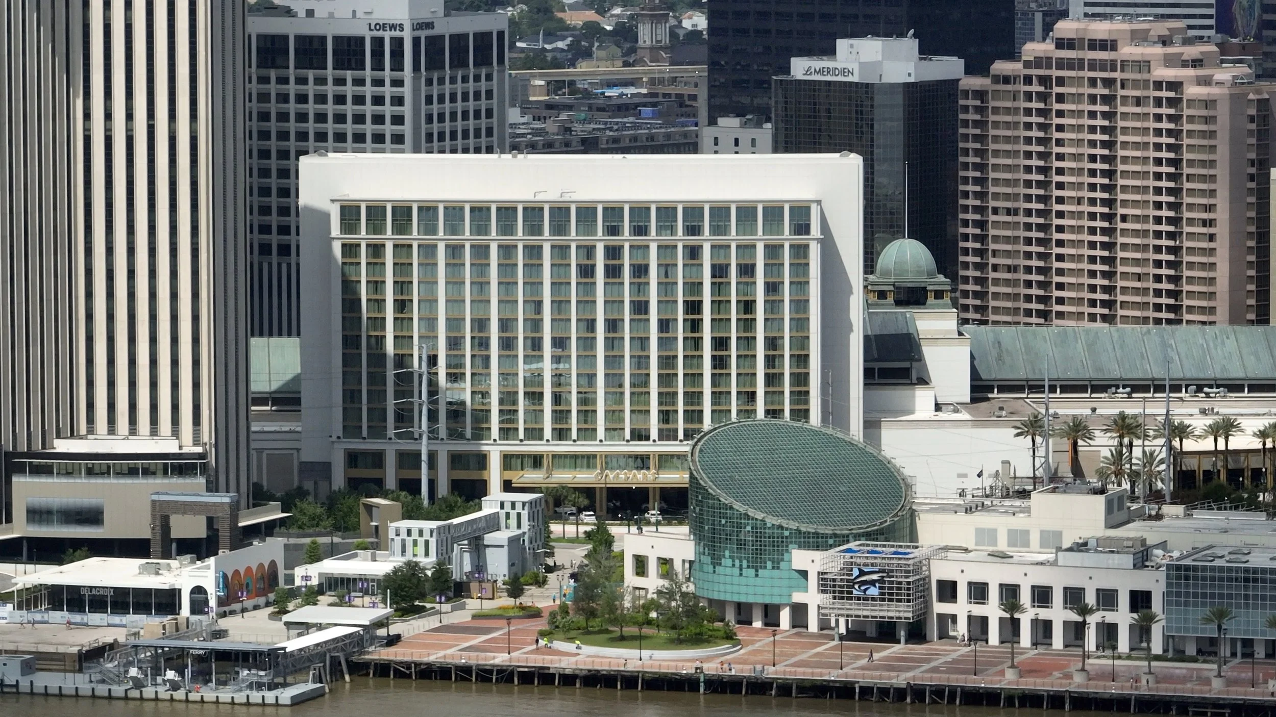 A city skyline with tall office buildings, a waterfront, palm trees, and a clear sky.