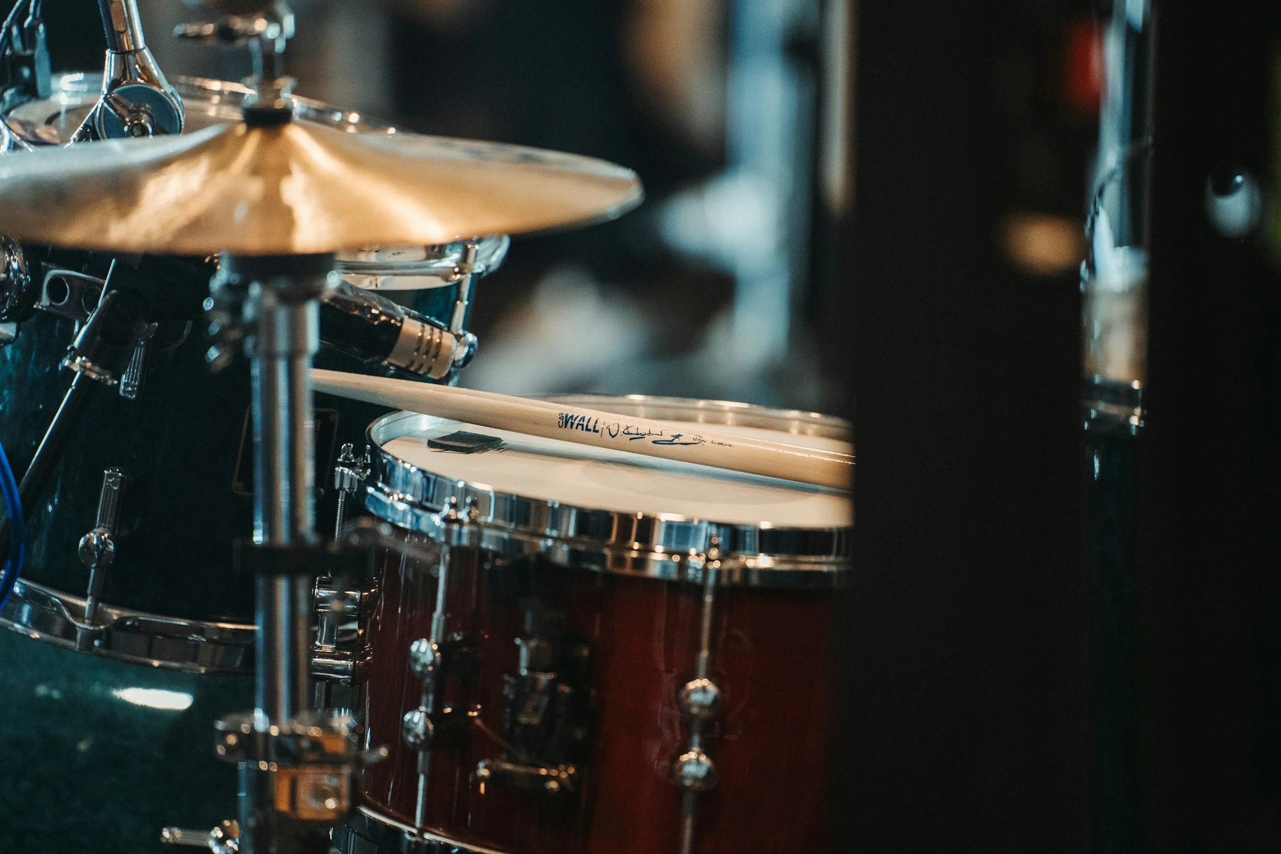 Close-up of a drum set, focusing on the snare drum, cymbal, and various hardware components in a dark setting.