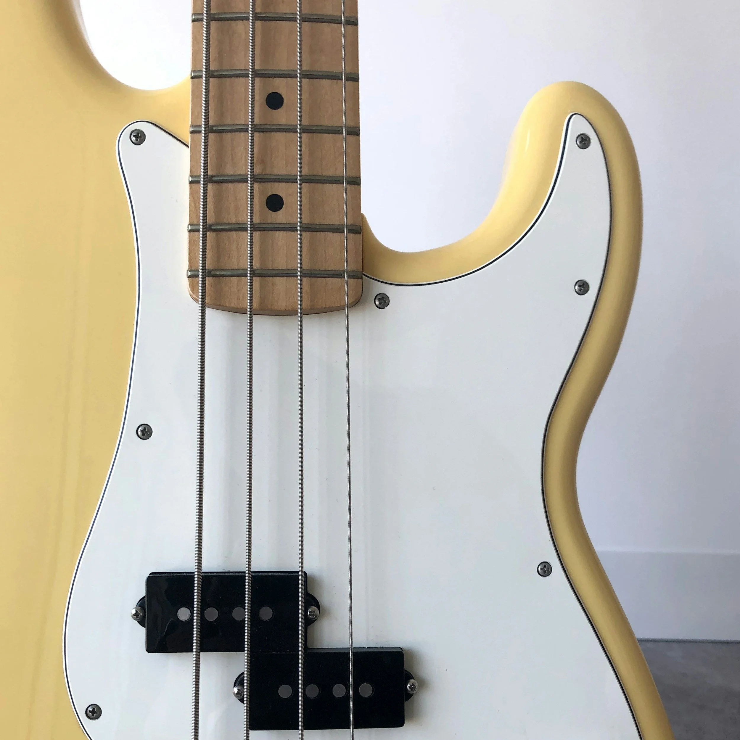 Close-up of an electric bass guitar's bridge and pickups, with metal strings, a yellow body, and a white pickguard.