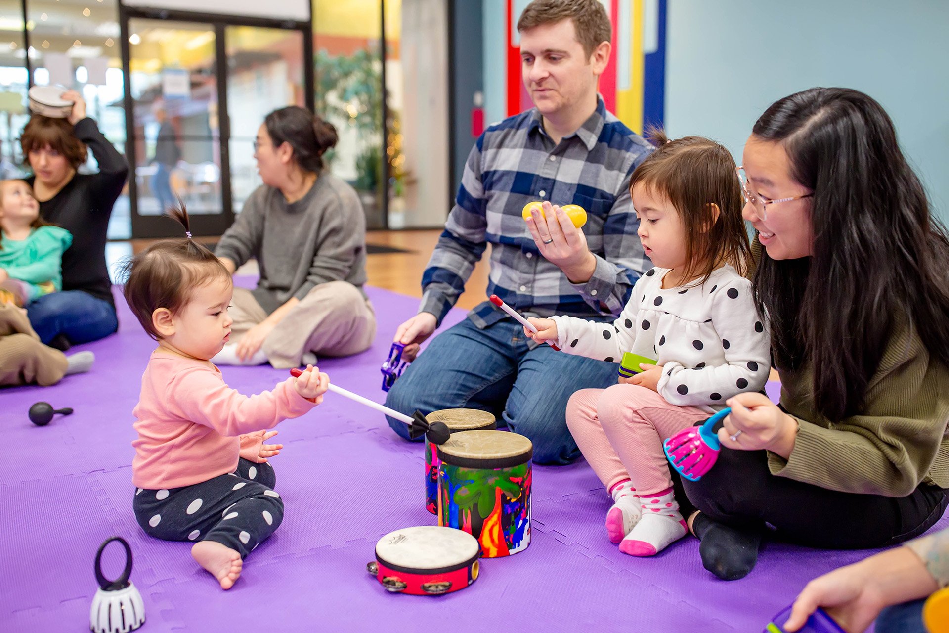 Young children sitting in a row, holding musical instruments in a classroom setting, with a girl in a yellow shirt in the foreground.