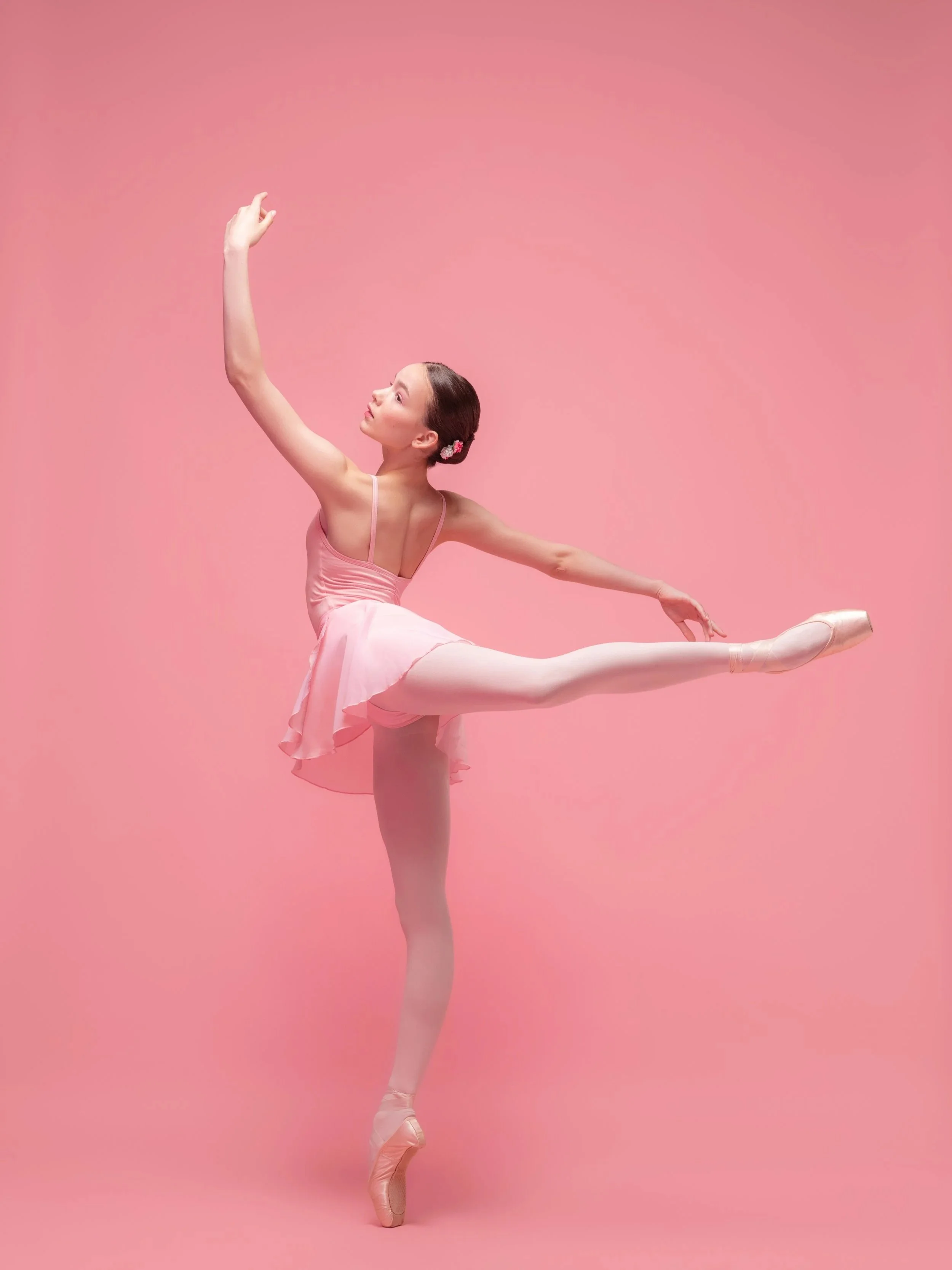 Two ballerinas dancing on stage with dark background, pink and purple lighting, one in a blue dress and another in a tutu.