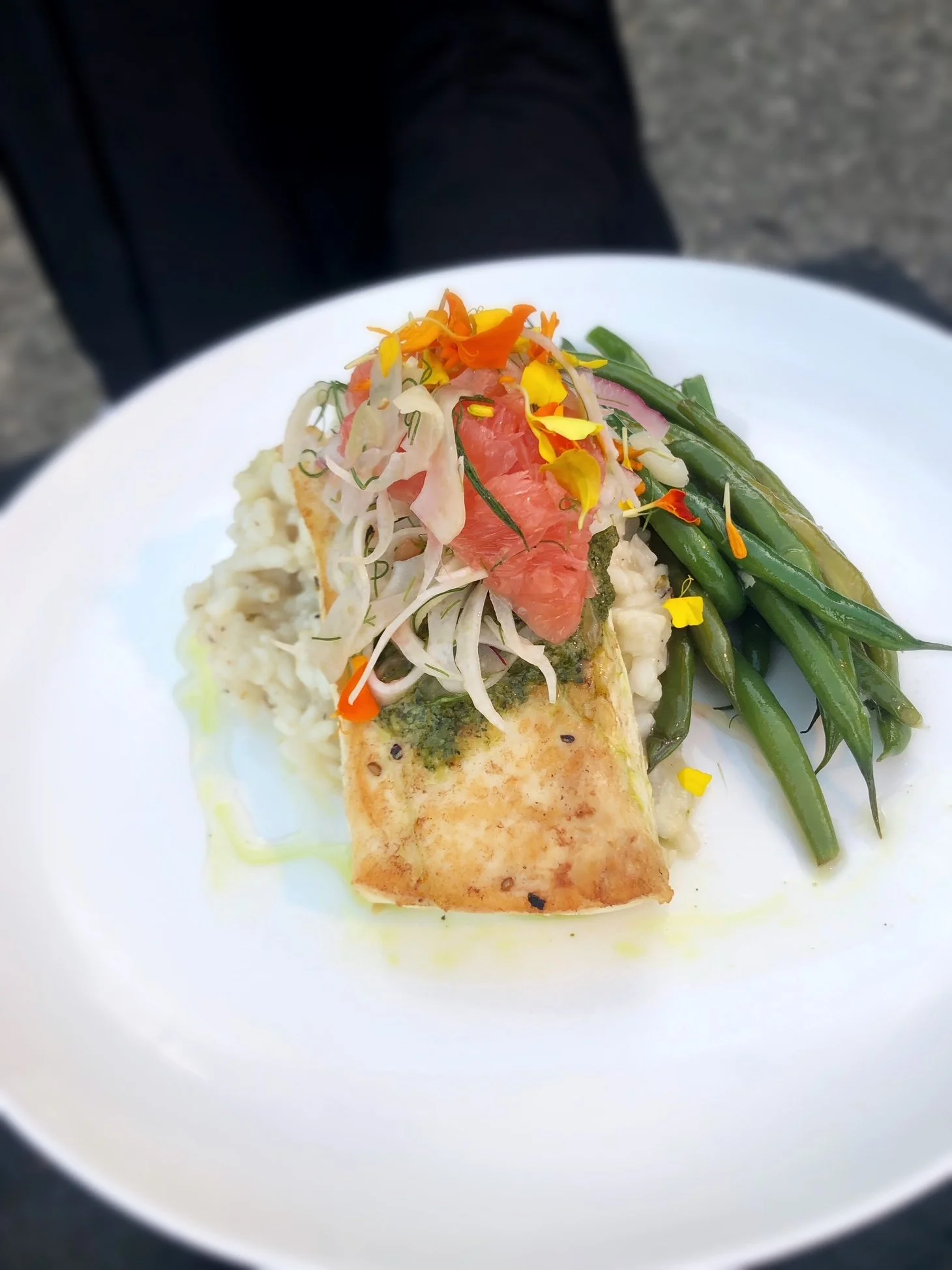 A plated dish featuring a grilled wrap with greens and grapefruit garnished with edible flowers, green beans, and potato salad.