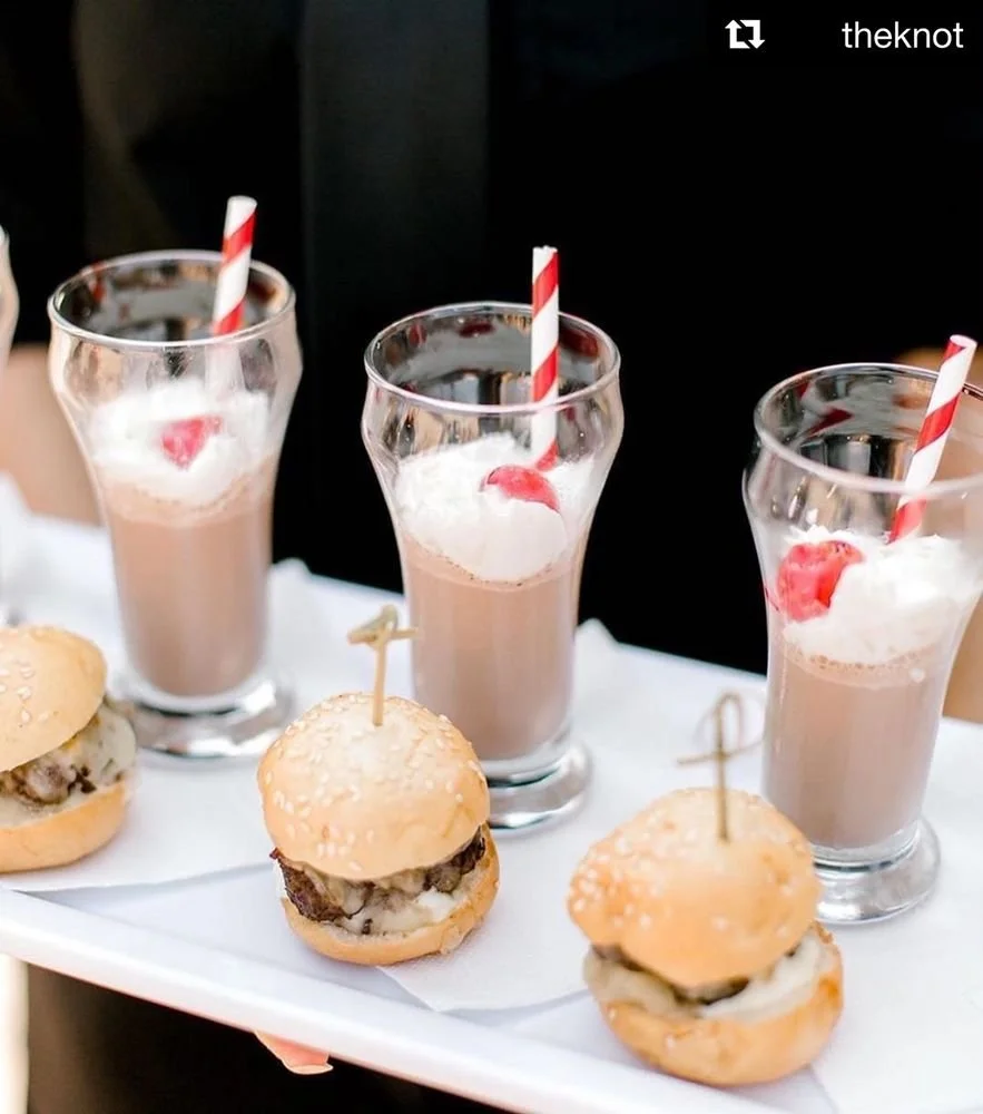 Three glasses of chocolate milkshake with whipped cream and cherry, three mini cheeseburgers on a tray.