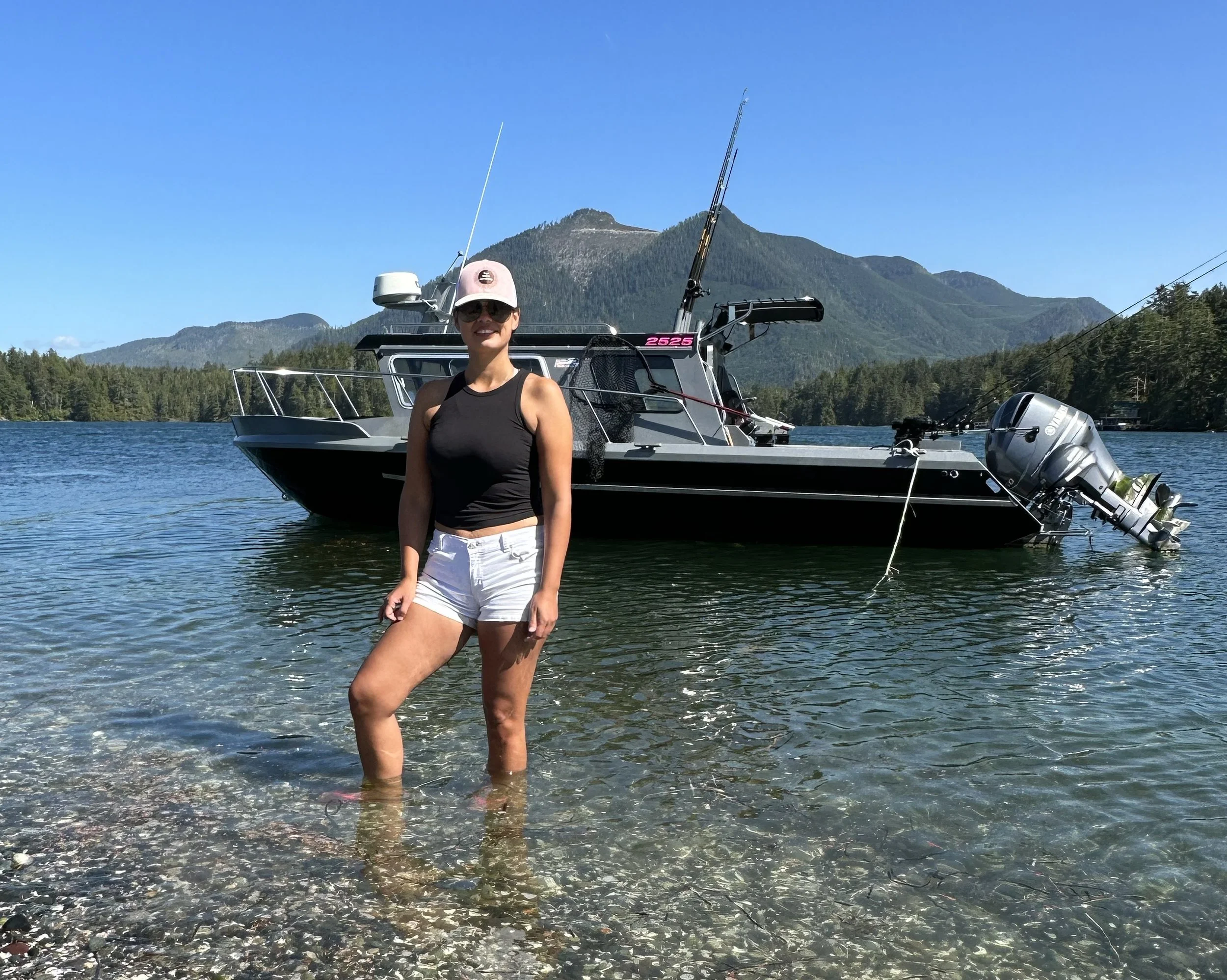 A woman standing in water near a boat with a mountain in the background on a clear, sunny day.