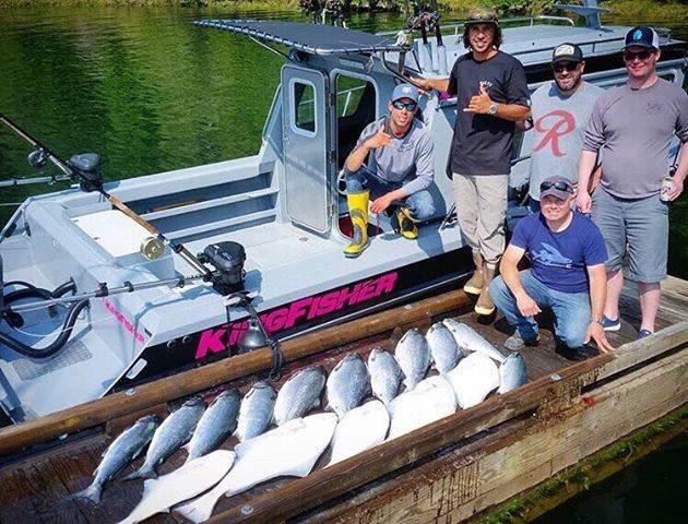 Five men on a dock with a small fishing boat named "King Fisher," displaying a catch of large fish laid out on the edge of the dock.