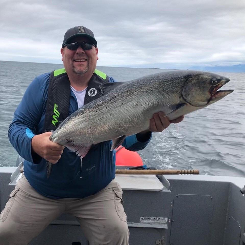 Man on boat holding large fish, smiling, outdoors on the water with cloudy sky.