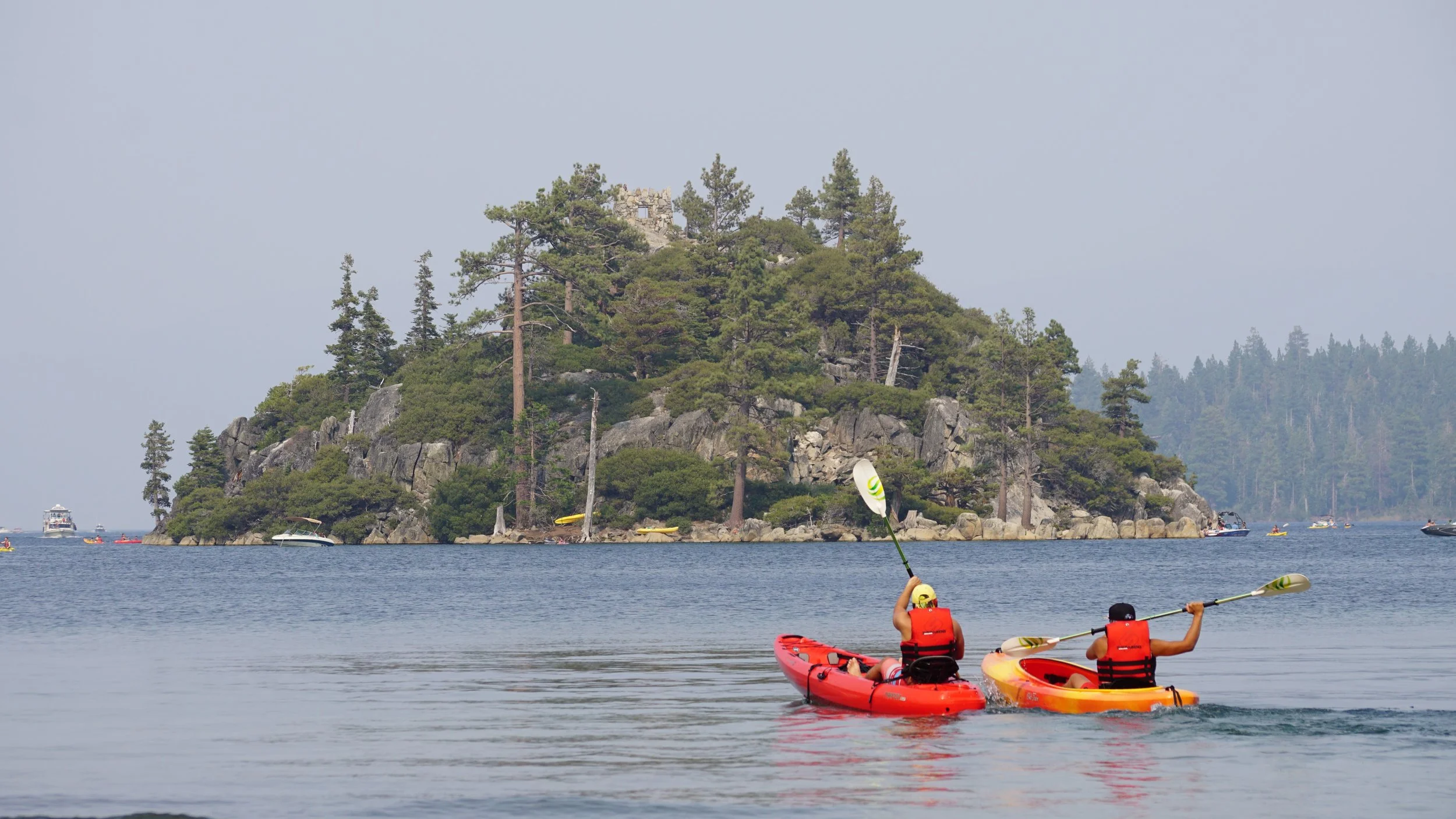 People kayaking on a body of water near a forested island with rocky cliffs and trees.