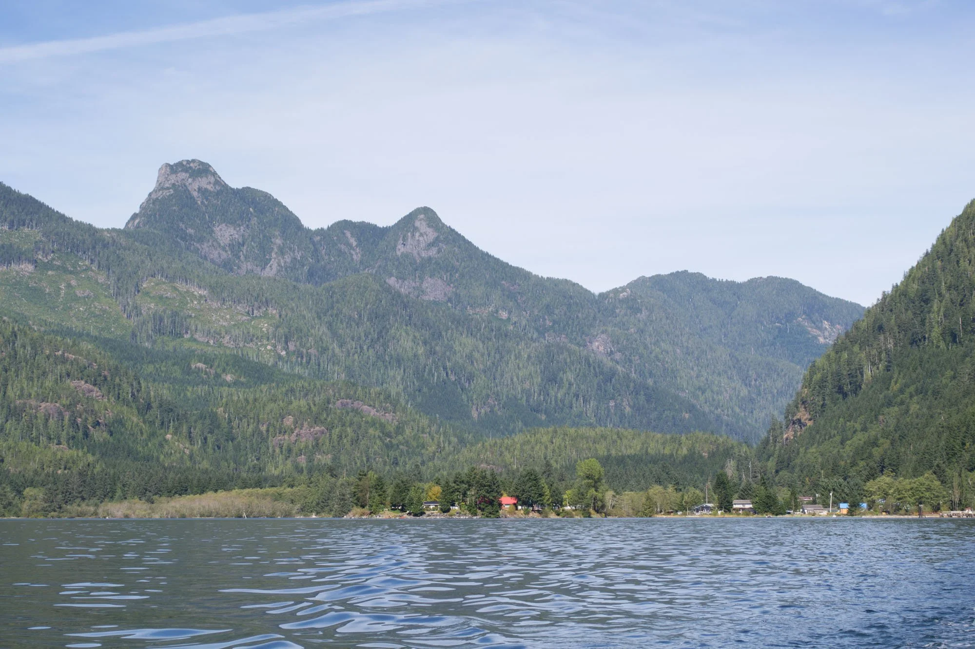 Scenic view of a mountain range with lush green forests, a lake in the foreground, and a clear blue sky.