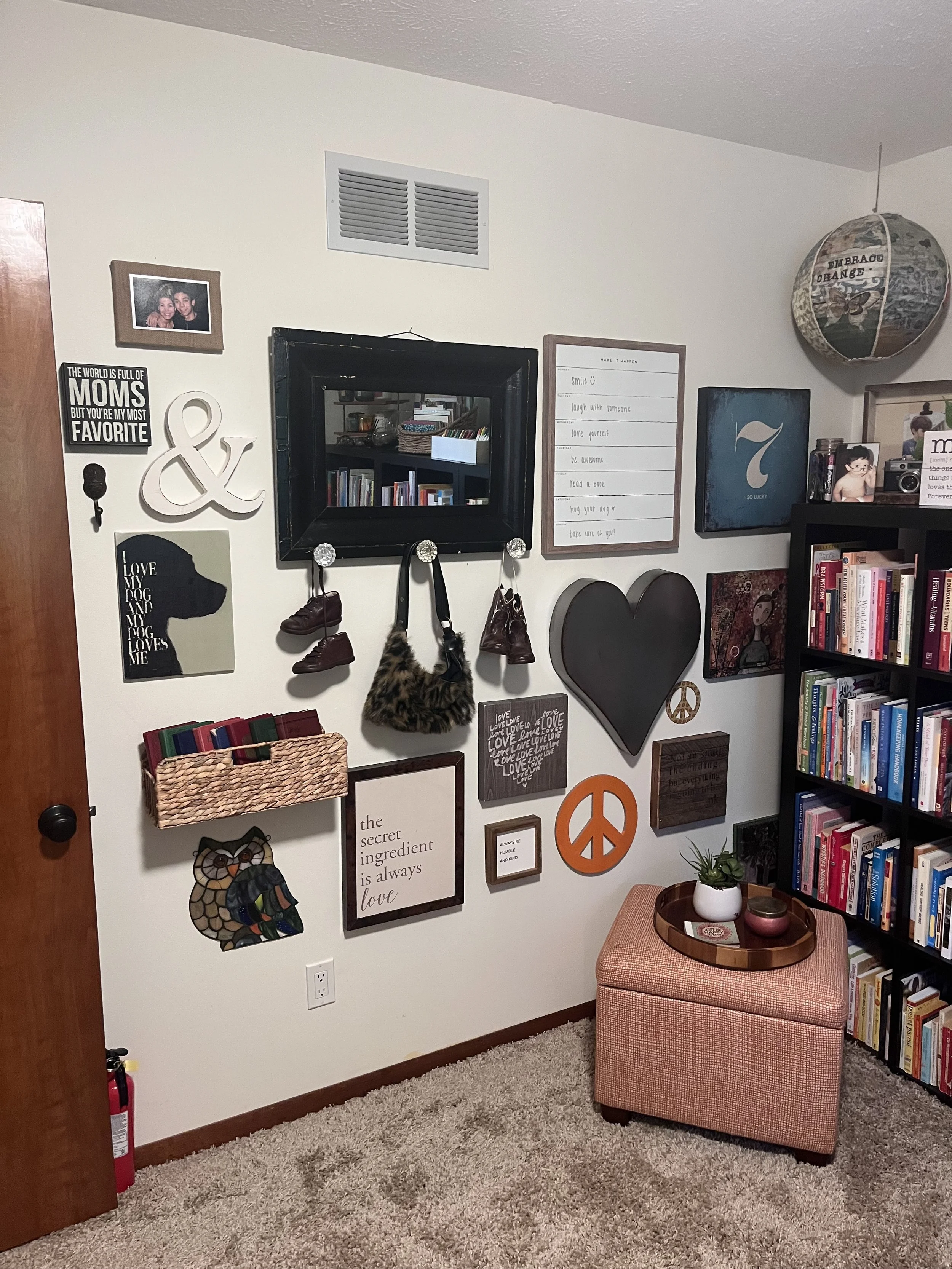 Decorated wall with picture frames, a mirror, shelves, inspirational signs, handbags, shoes, and artwork in a living room corner.