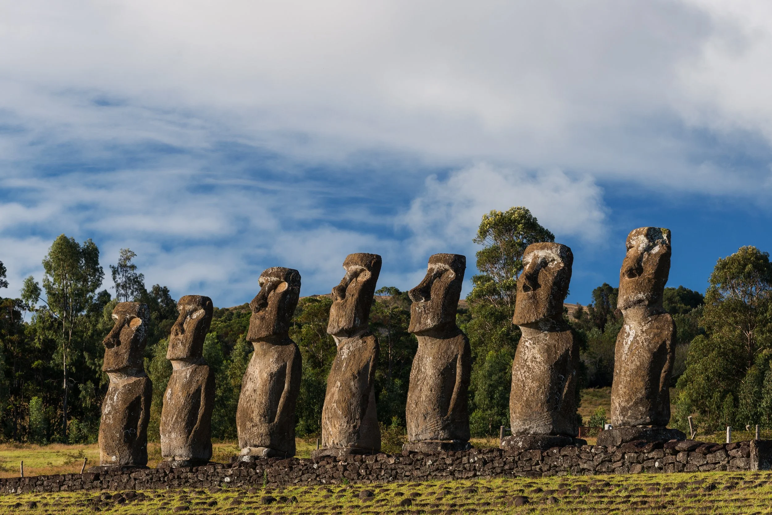 Siete estatuas moáis en Isla de Pascua, Chile, con cielo azul y nubes.