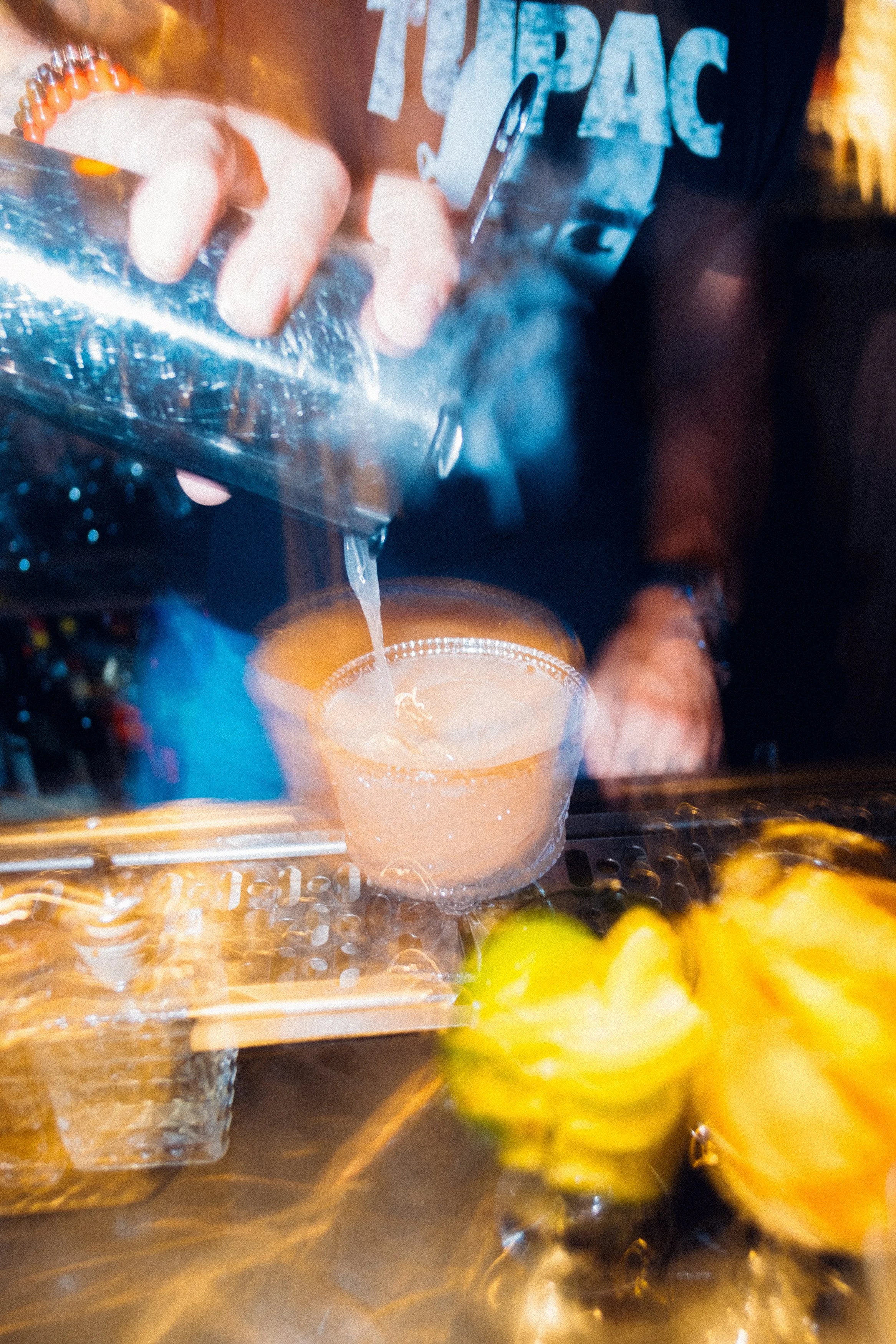 A bartender pours a pink cocktail into a glass at a bar.