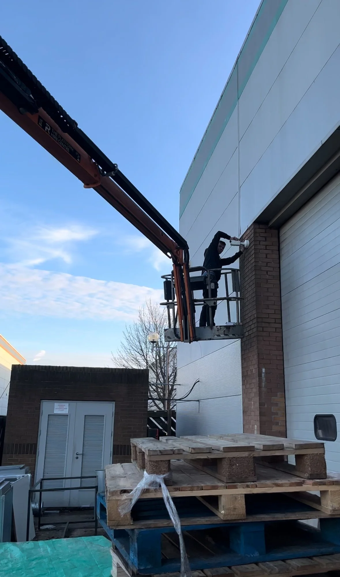 A person working on installing or maintaining a security camera on the exterior of a building using a cherry picker.