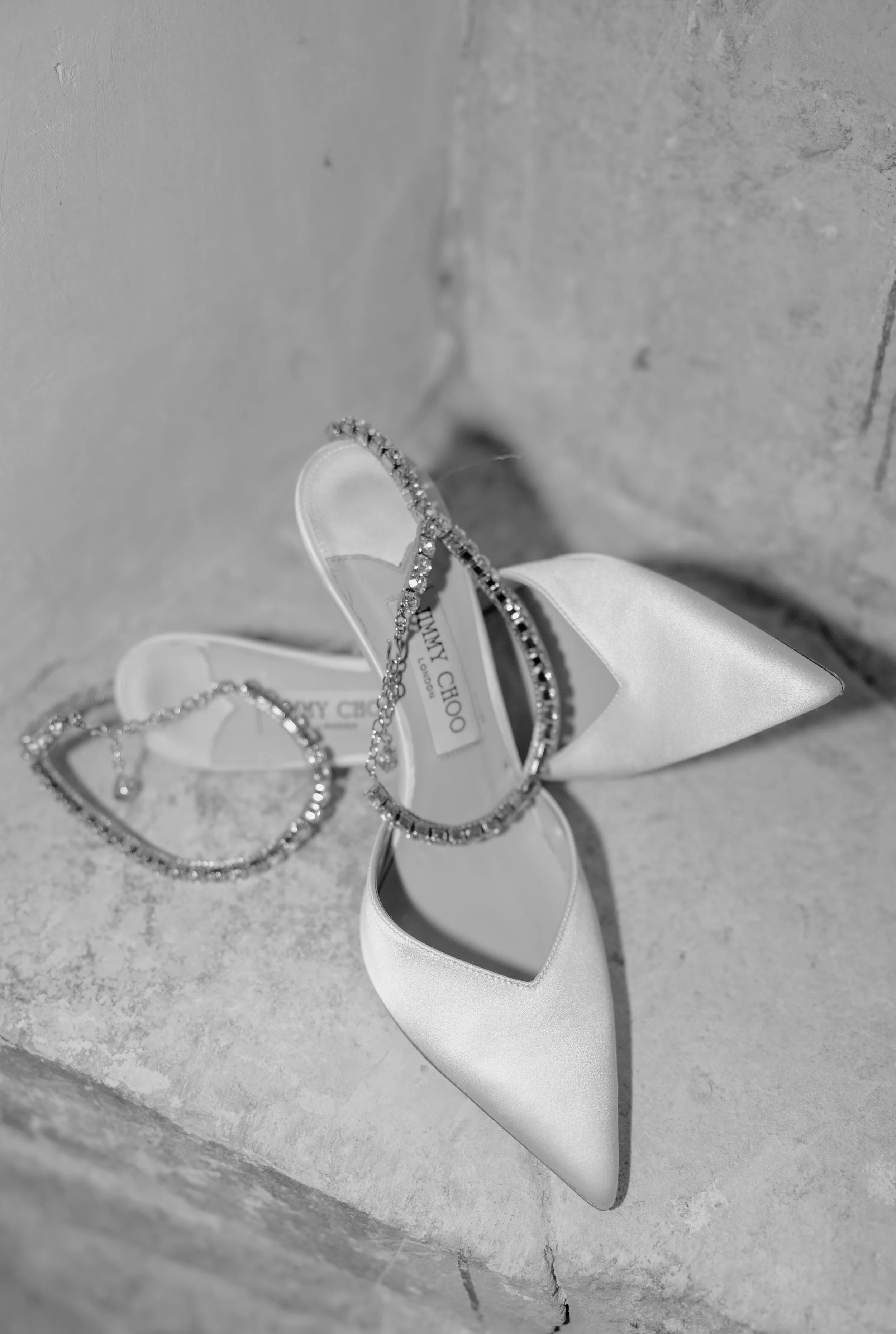 A pair of diamond jewelry pieces, possibly earrings or necklaces, resting on a white ribbon or decorative shoe set against a textured wall background.