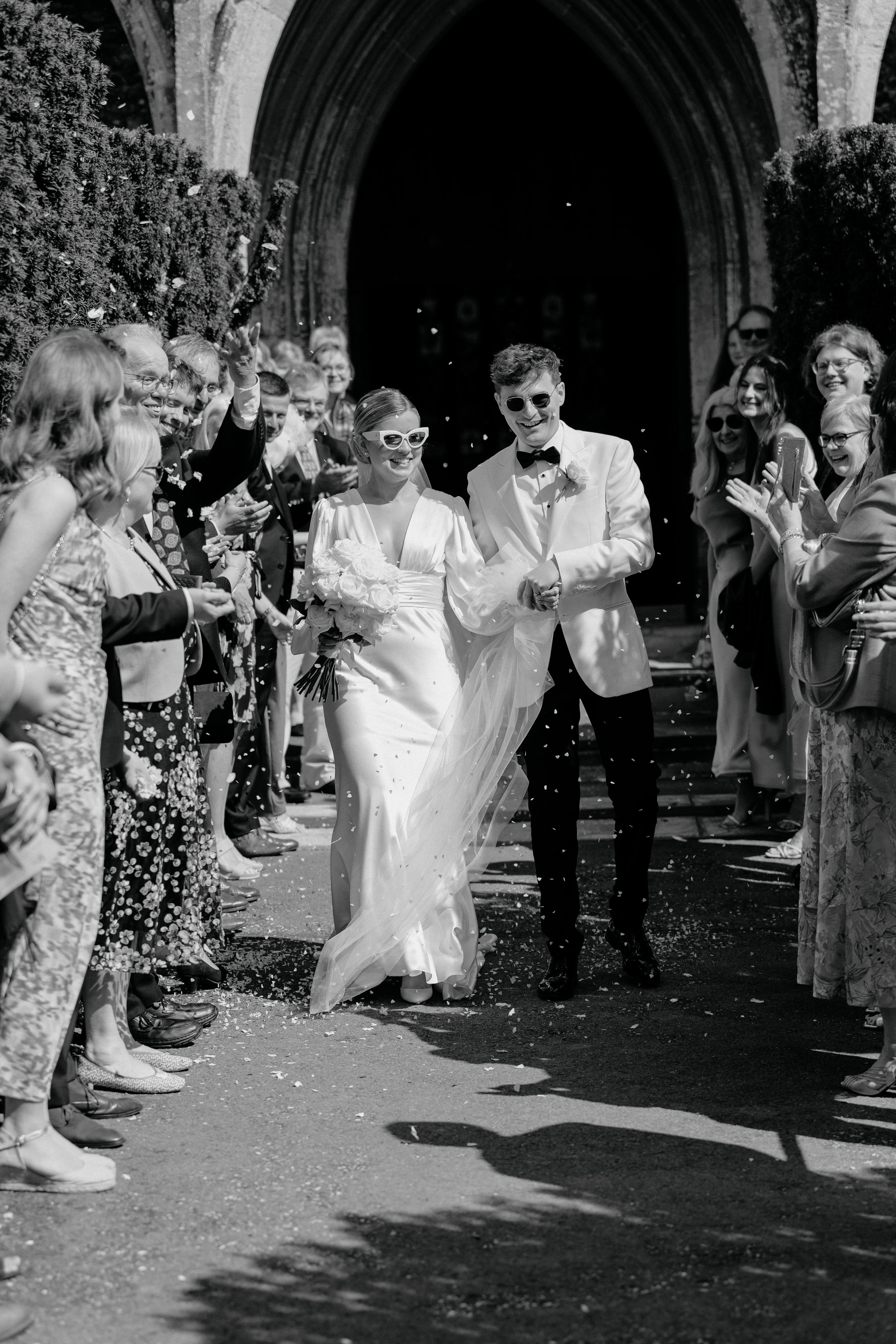 Bride and groom walking through wedding guests wearing shades