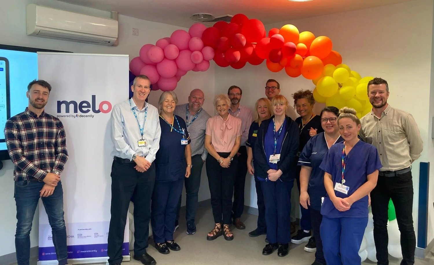 Members of the Melo team with hospital staff, standing under a balloon arch