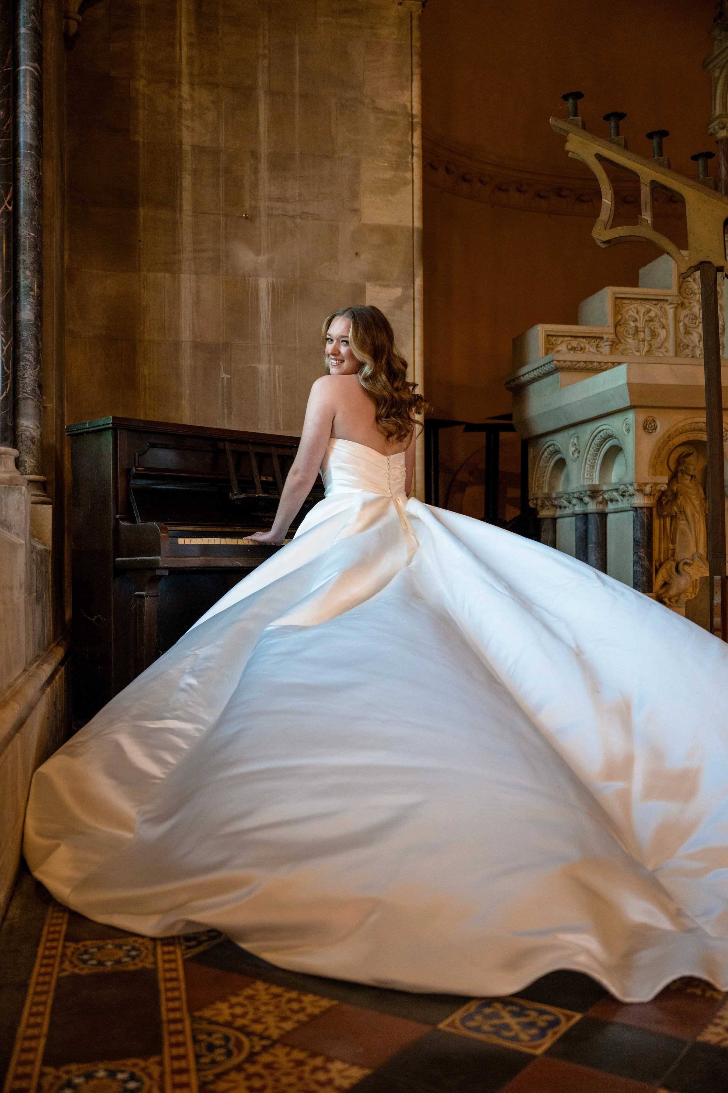 A woman in a white wedding dress sitting at a piano in a historic church or cathedral with ornate architectural details.