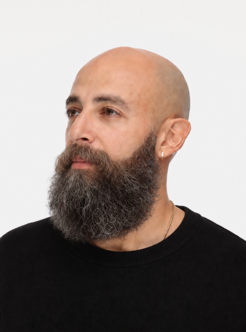 A bald man with a full gray and brown beard, wearing a black sweater and a small gold necklace, looking to the side against a plain white background.