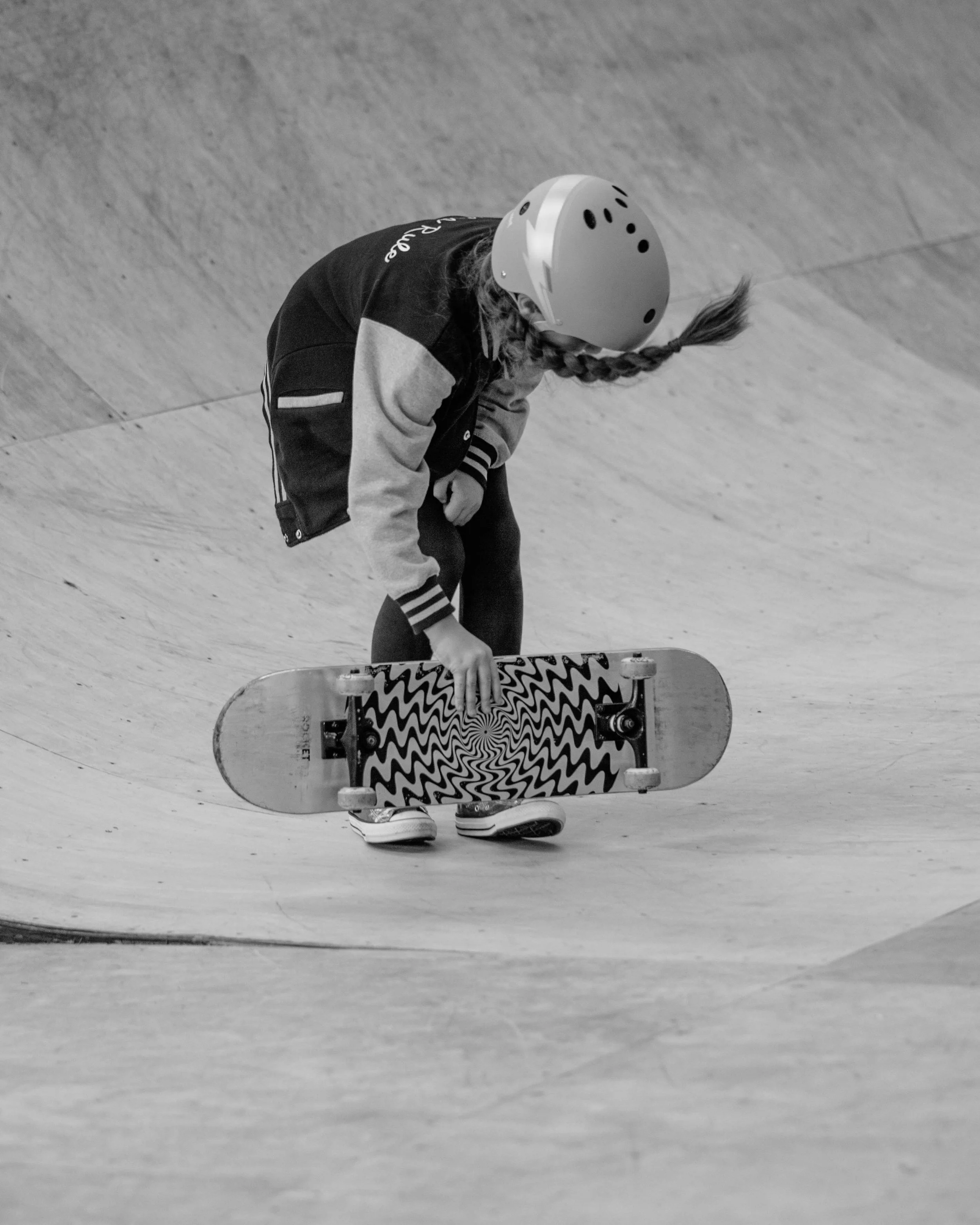 A young girl with a helmet kneeling on a skateboard in a skate park.