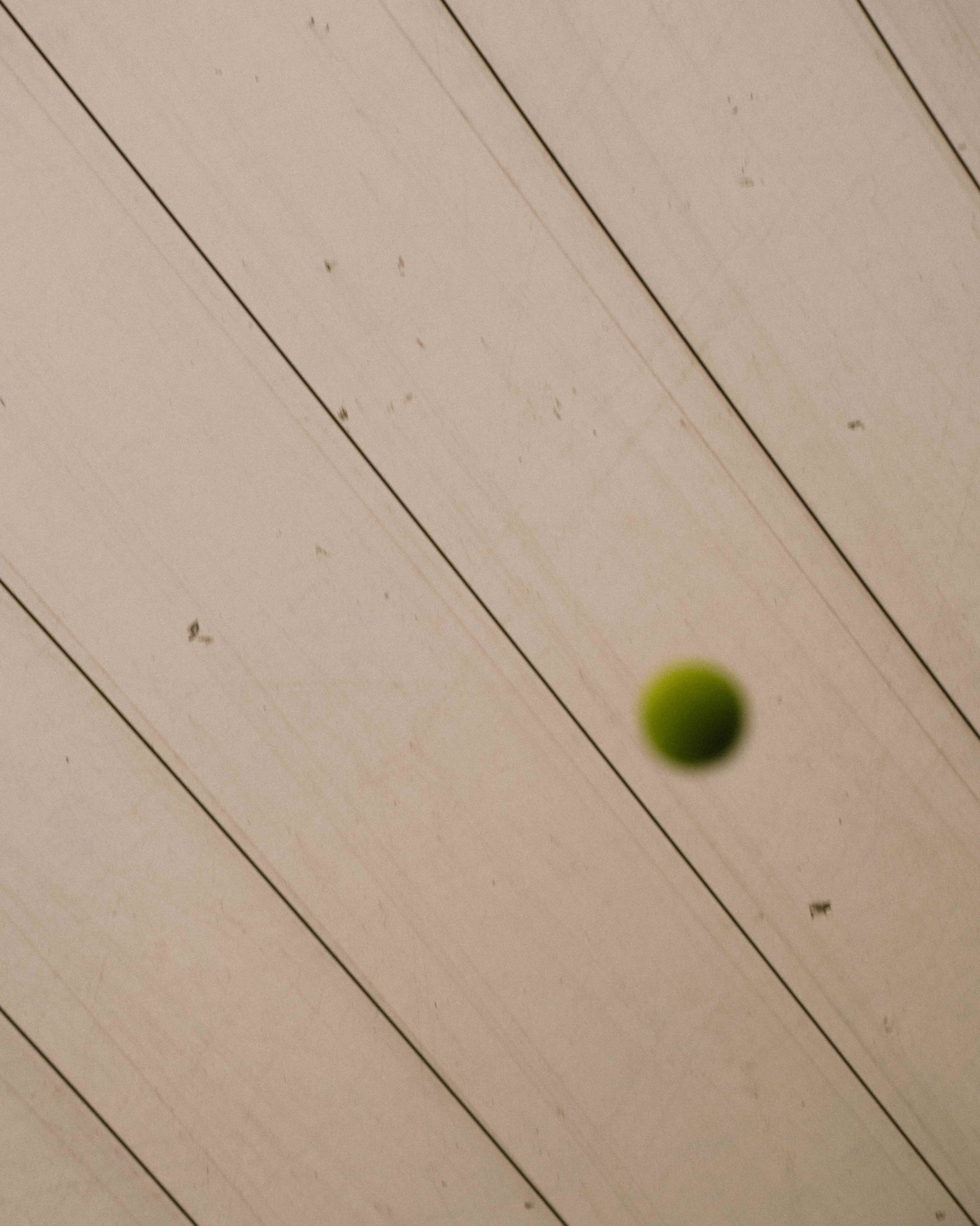 A green tennis ball in mid-air against a ceiling with wooden panels.